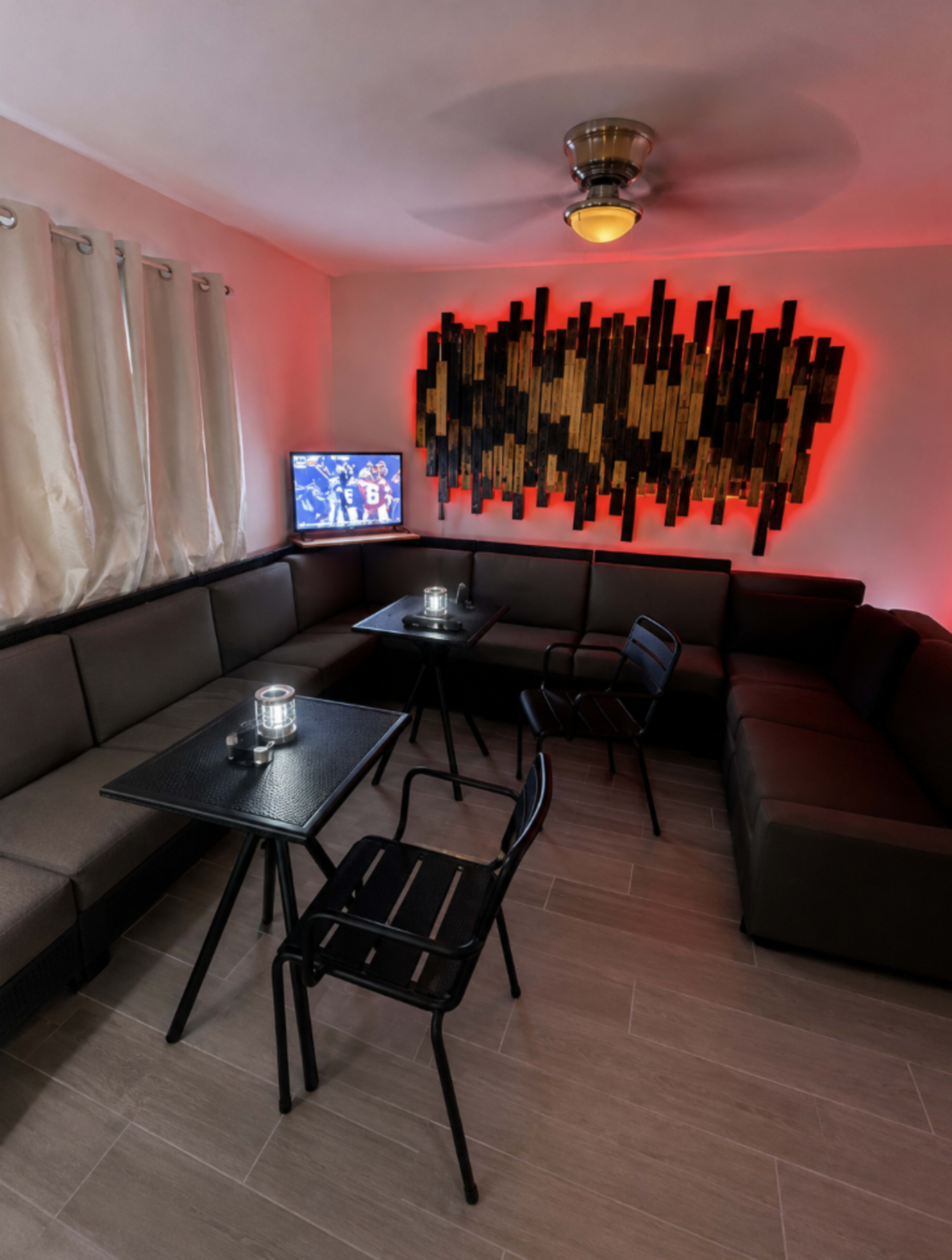 A cozy lounge area features sectional seating, a television against a wall with artistic panels, and tables with chairs arranged for conversation.