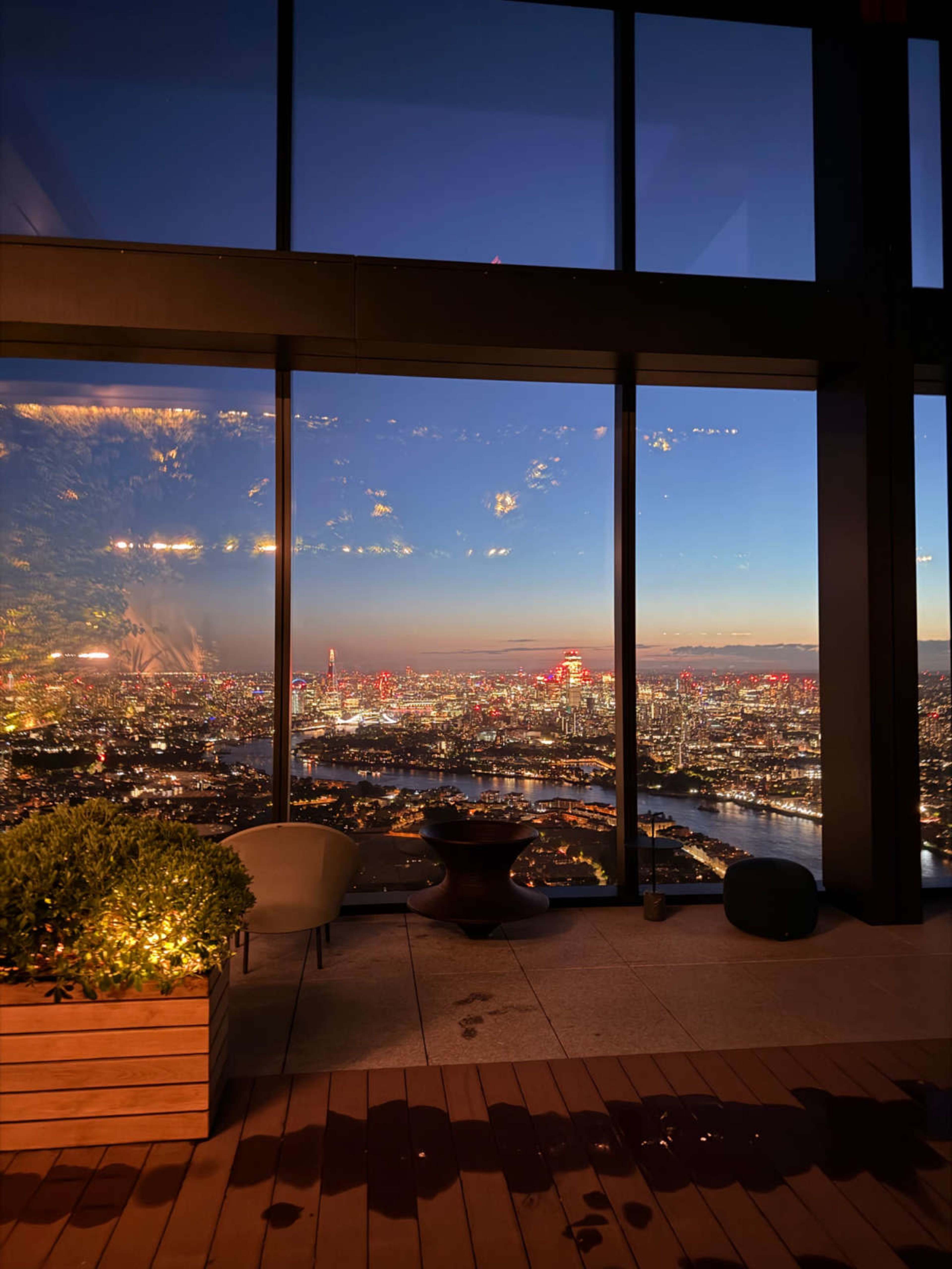 The image shows a panoramic view of a city skyline at dusk, with colorful lights reflecting off buildings and a river visible below.