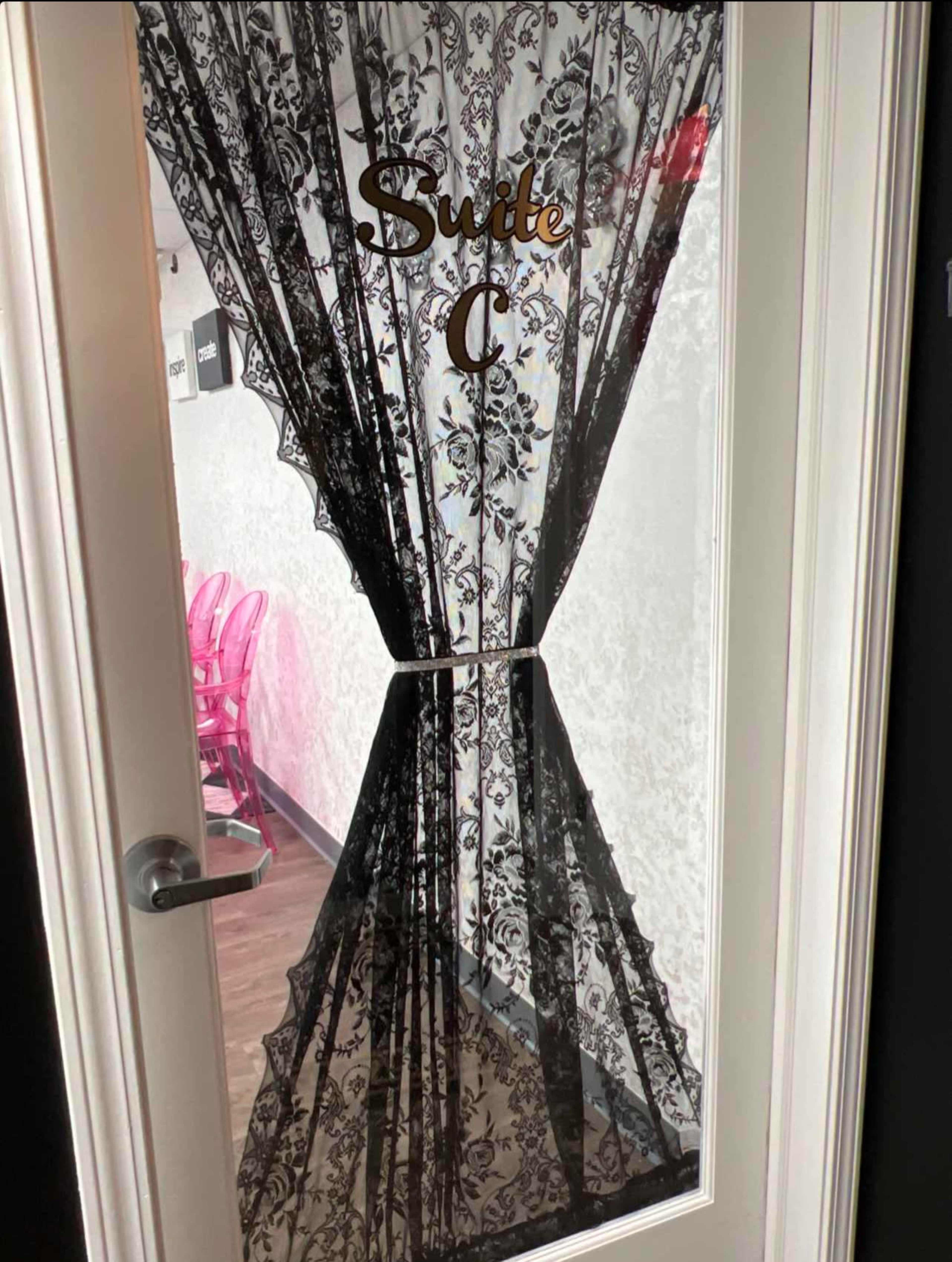 The image shows a door with a lace curtain labeled "Suite C," revealing a glimpse of a room with pink chairs inside.