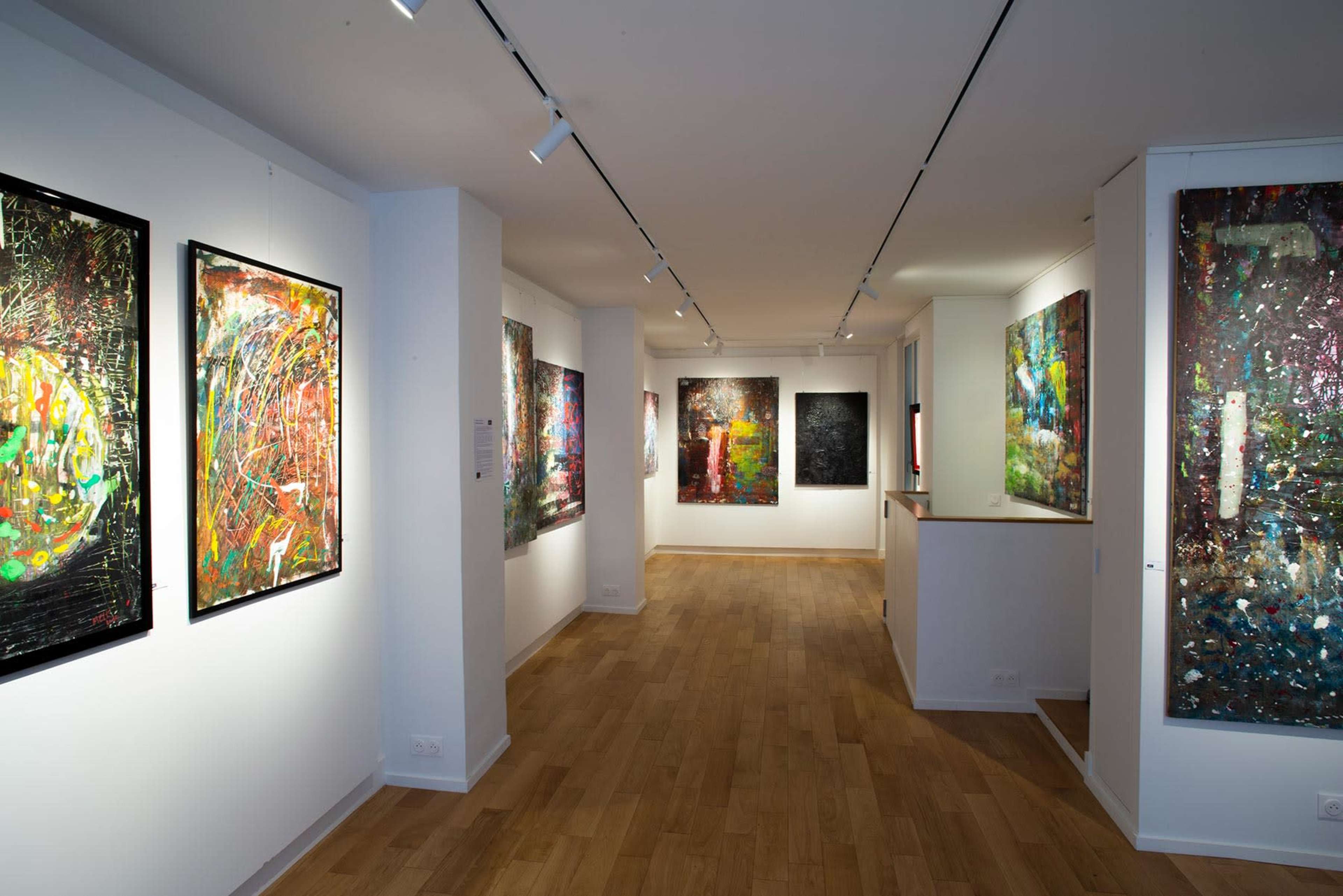 A modern art gallery featuring brightly colored abstract paintings on white walls and wooden flooring.