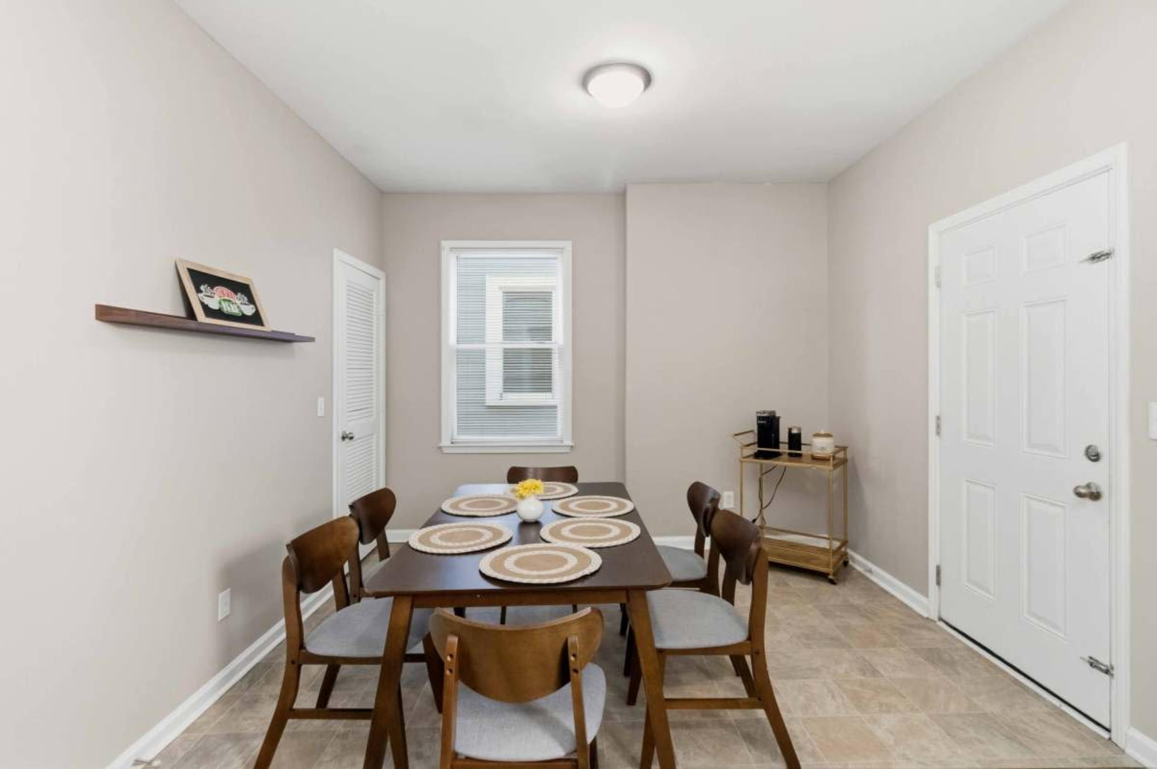 A dining area features a wooden table surrounded by chairs, a shelf on the wall, and a door leading outside.