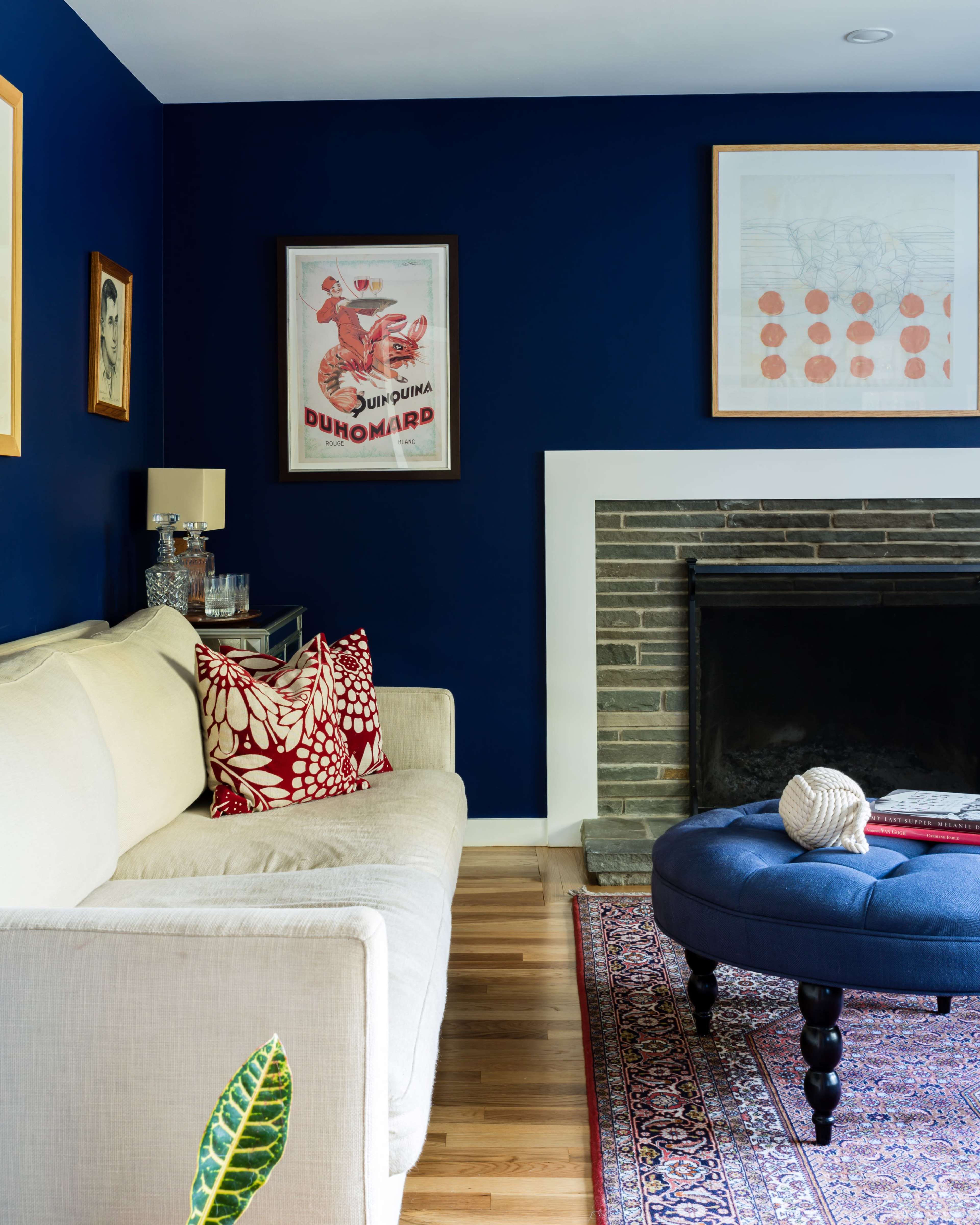 The image shows a cozy living room featuring a white sofa with decorative pillows, a blue wall, a fireplace with a stone facade, and various artworks hung above.