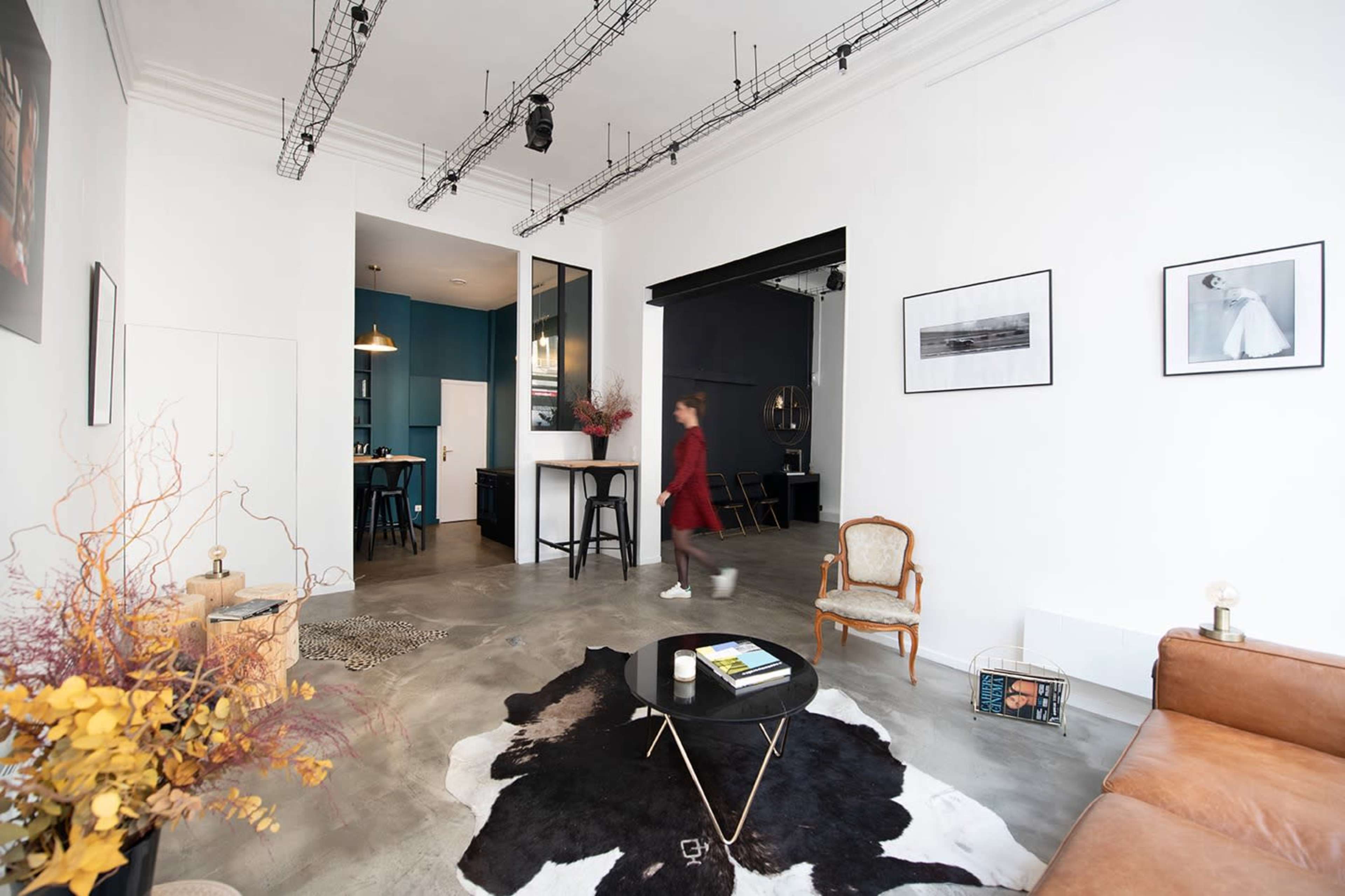 A spacious room features a mix of modern furnishings, including a brown leather sofa, a black and white cowhide rug, and various framed artworks on the white walls.