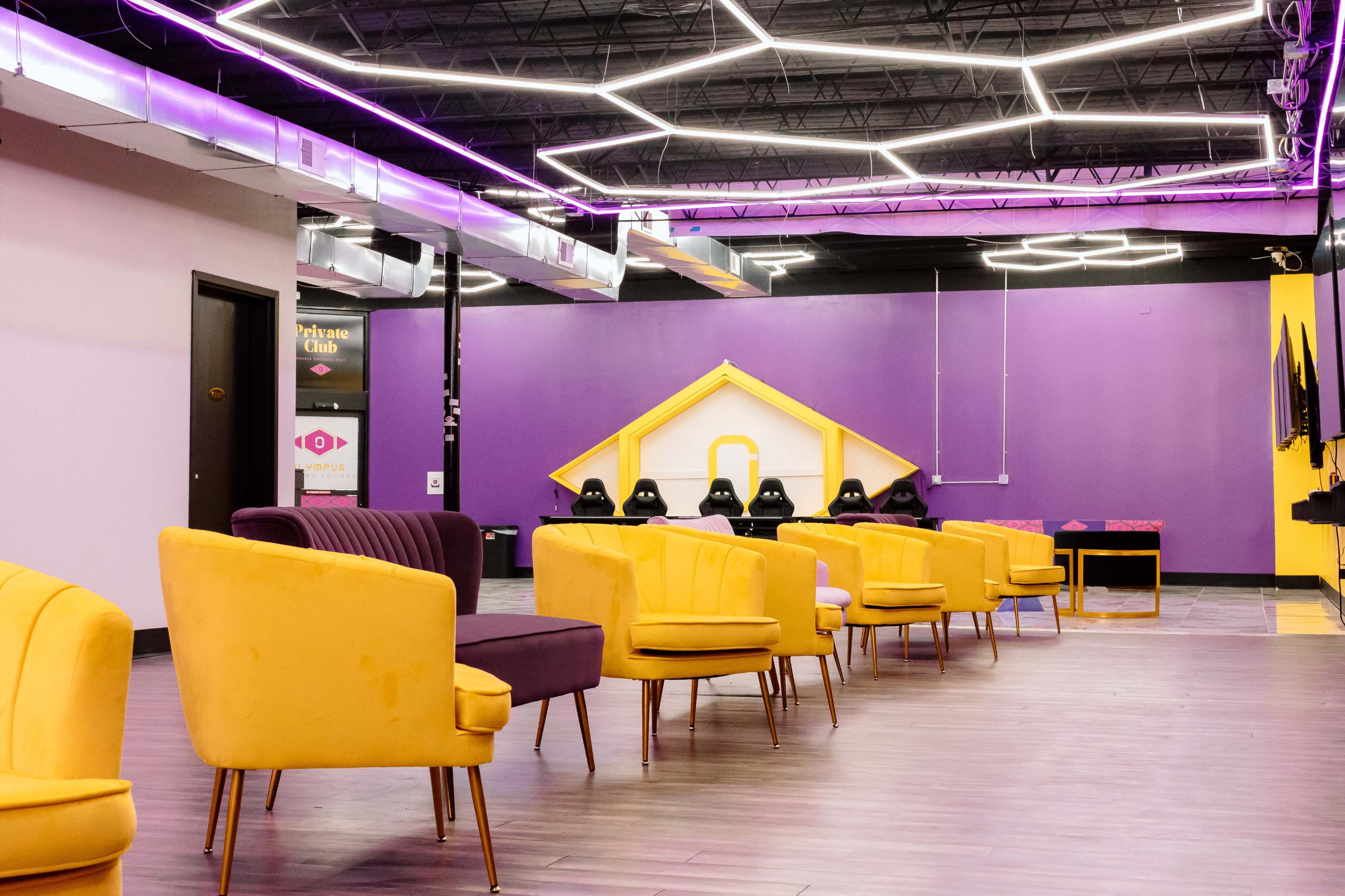 The image shows a modern lounge area with colorful seating arranged in a spacious room featuring purple and yellow walls and decorative lighting.