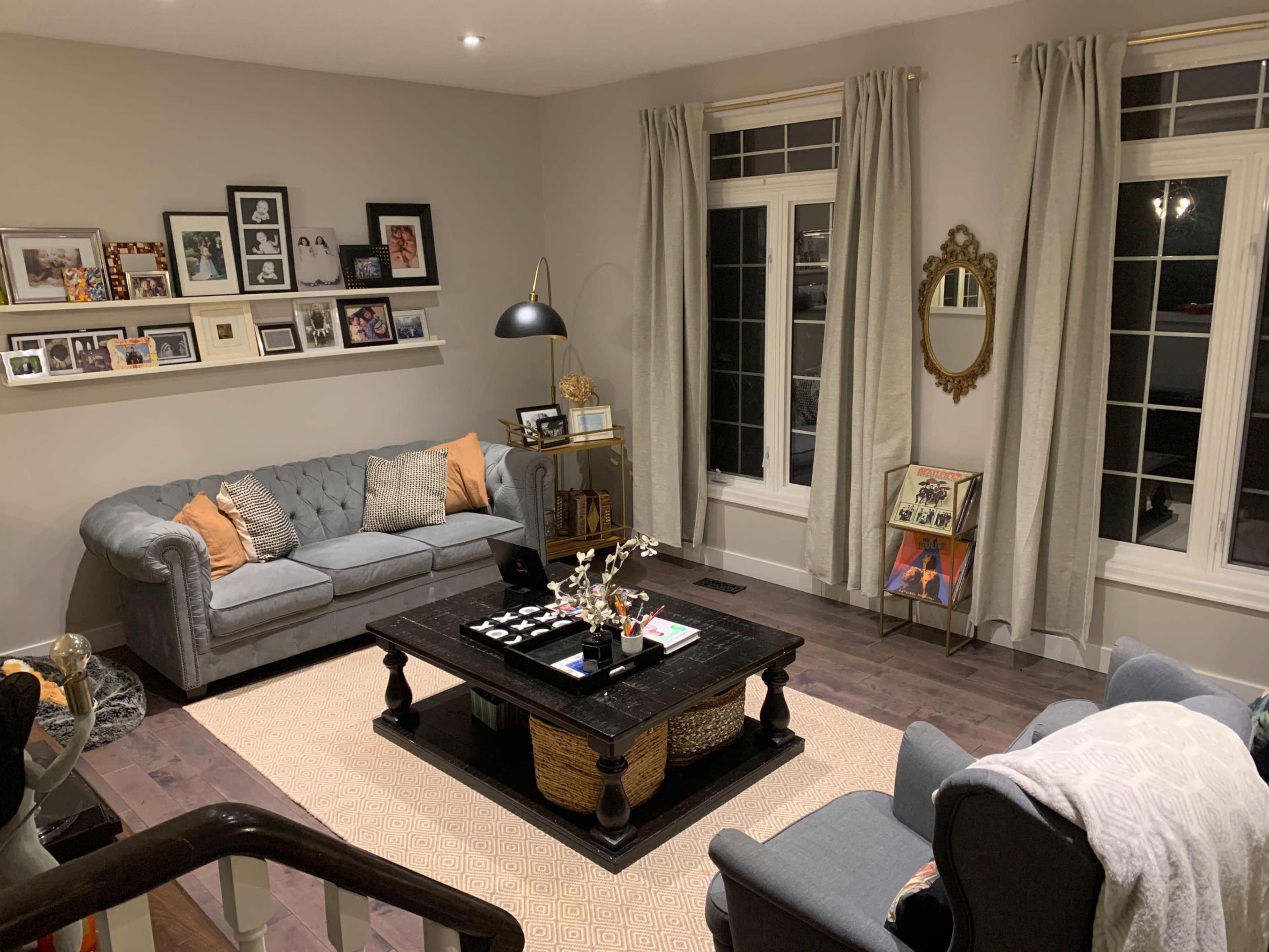 The image shows a cozy living room featuring a gray couch, a coffee table with decorative items, a woven rug, and framed photographs on the wall.