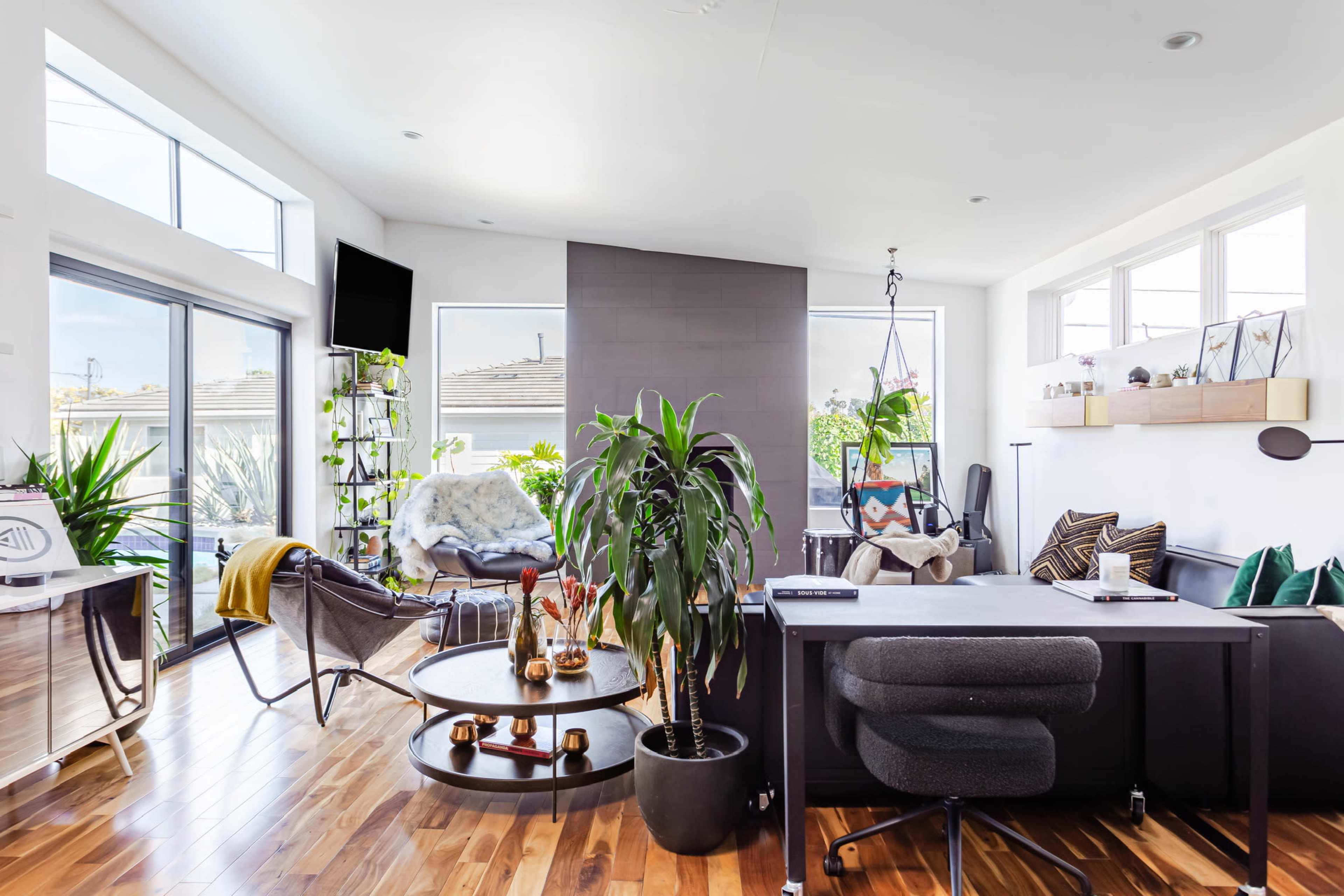 A modern interior space features a home office with a round coffee table, large windows, indoor plants, and a cozy seating area.