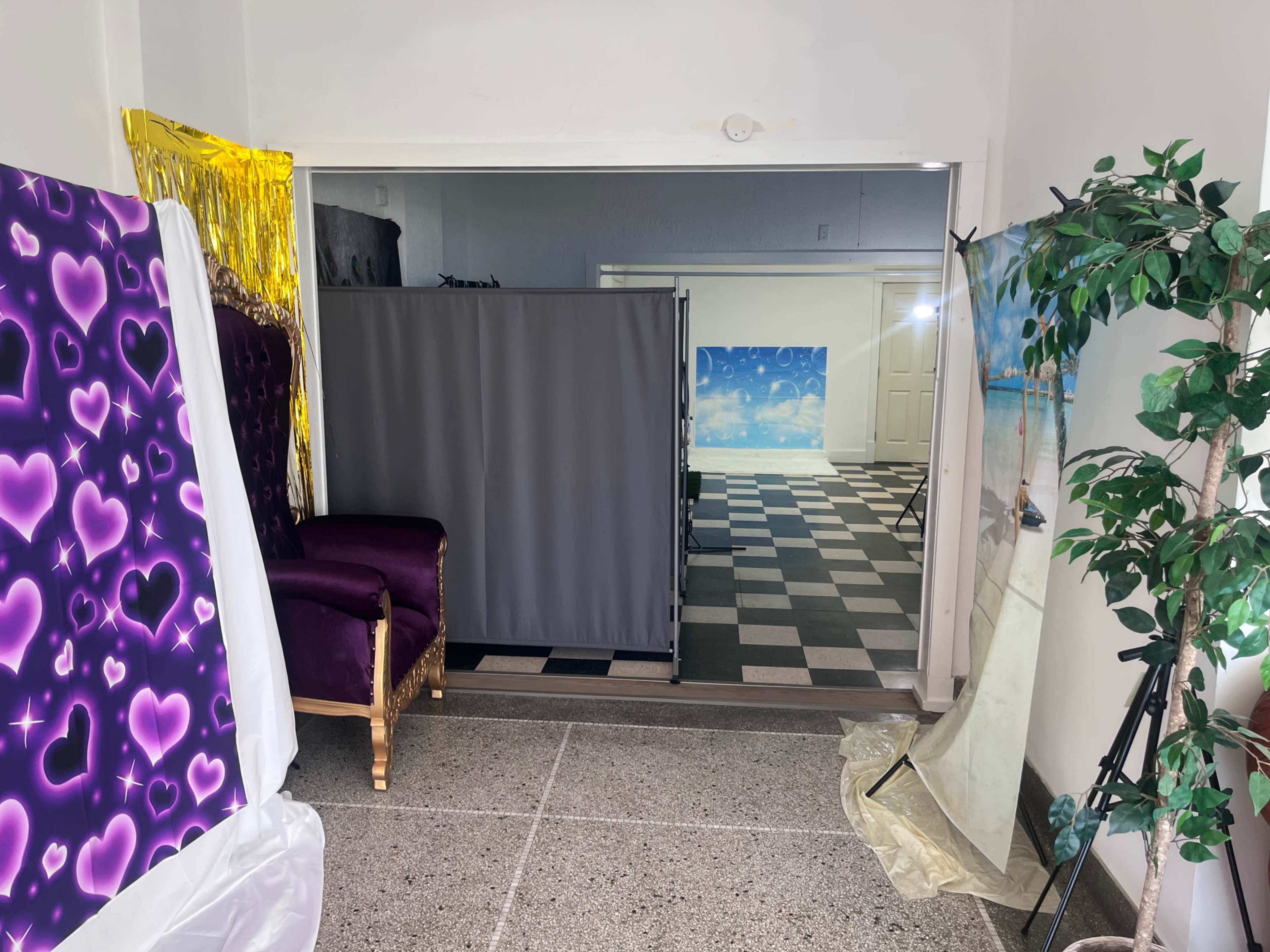 The image shows a room featuring a purple chair with gold accents, a gray divider, and various backdrops on display, including one with a blue sky.