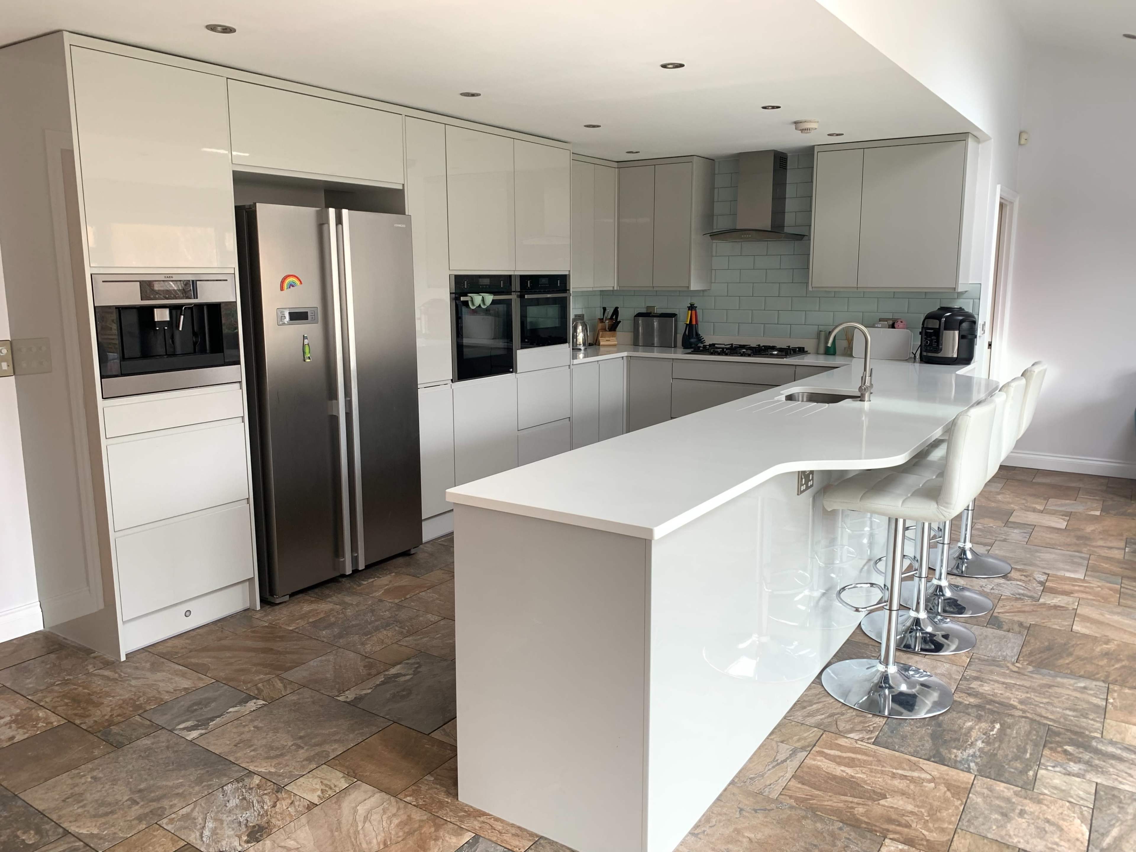 A modern kitchen features gray cabinetry, stainless steel appliances, a large island with bar stools, and a tiled floor.