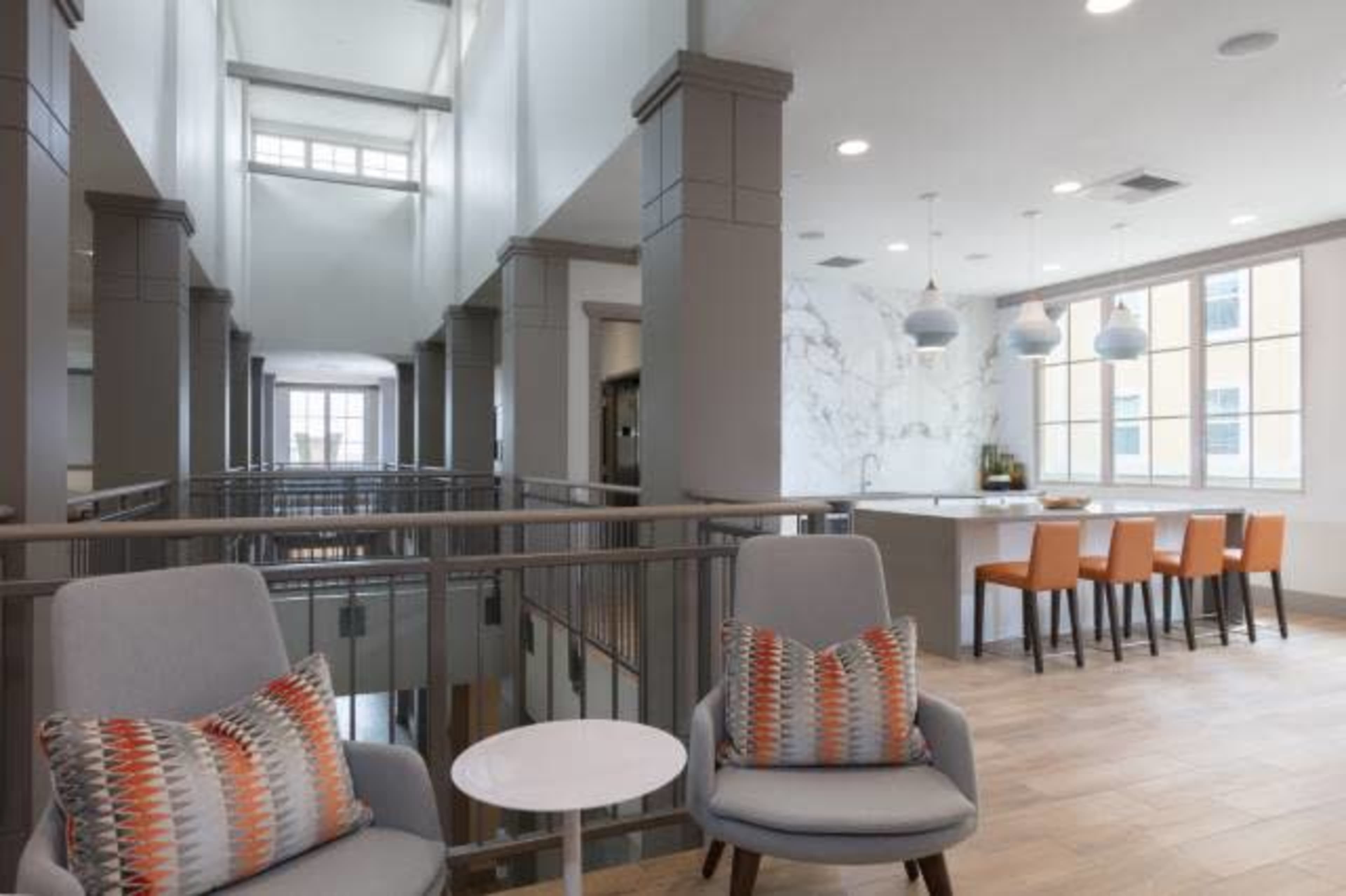 A spacious, modern interior featuring a lounge area with two chairs and a small table, overlooking a kitchen with bar seating and large windows.