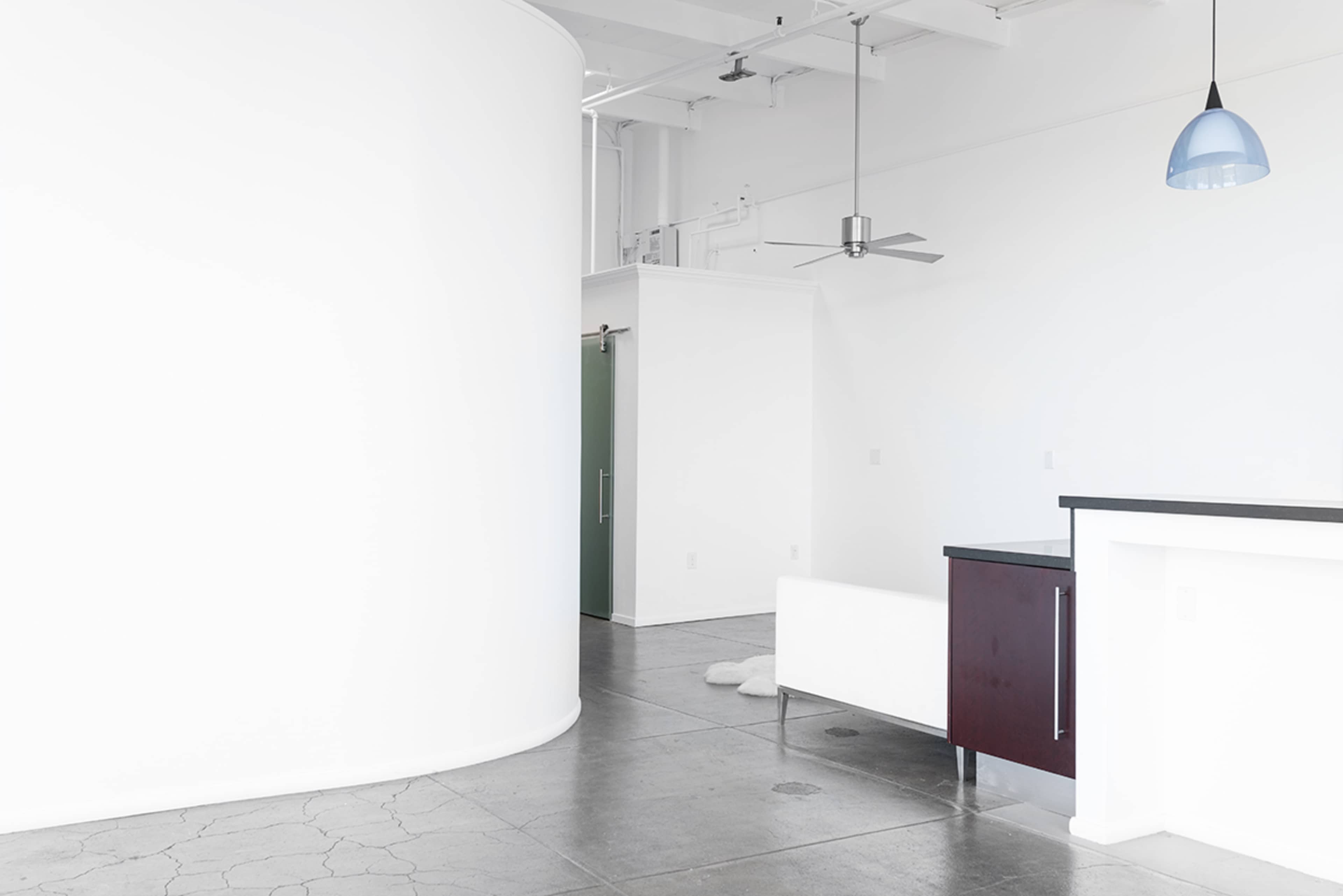 A spacious, minimalist interior with a curved white wall, a green door, and a dark countertop.