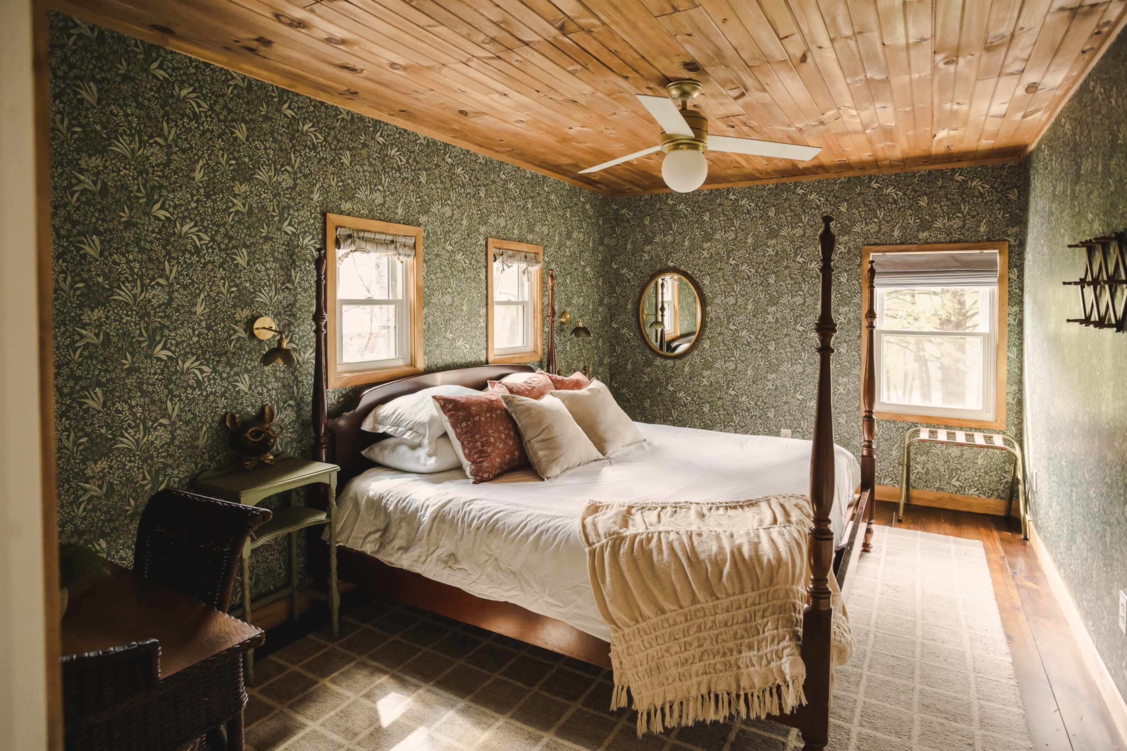 The image shows a well-lit bedroom with a four-poster bed, patterned wallpaper, and a wooden ceiling.