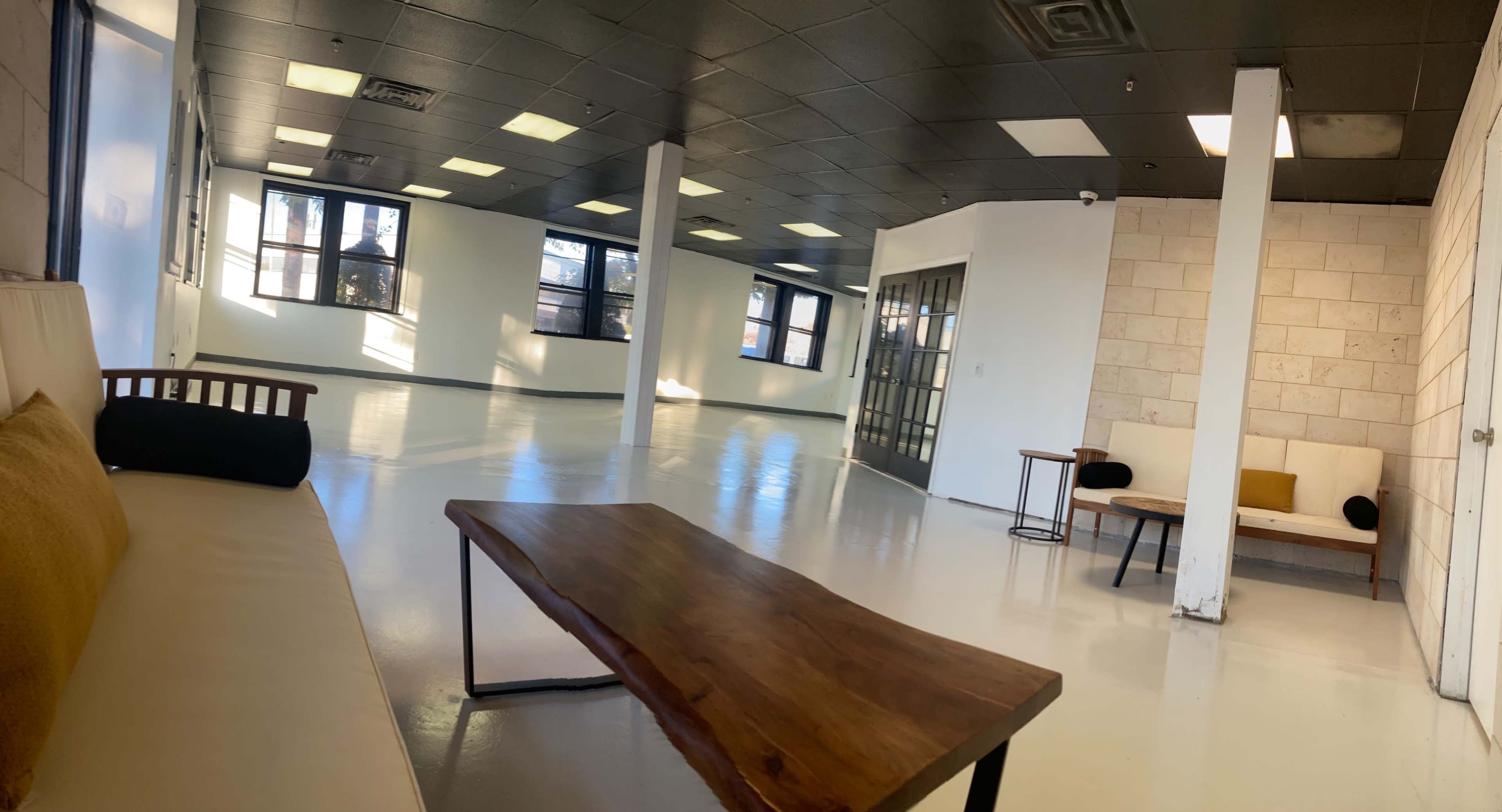 A large, empty room with a polished white floor, featuring minimalist furniture, large windows, and a partitioned area.