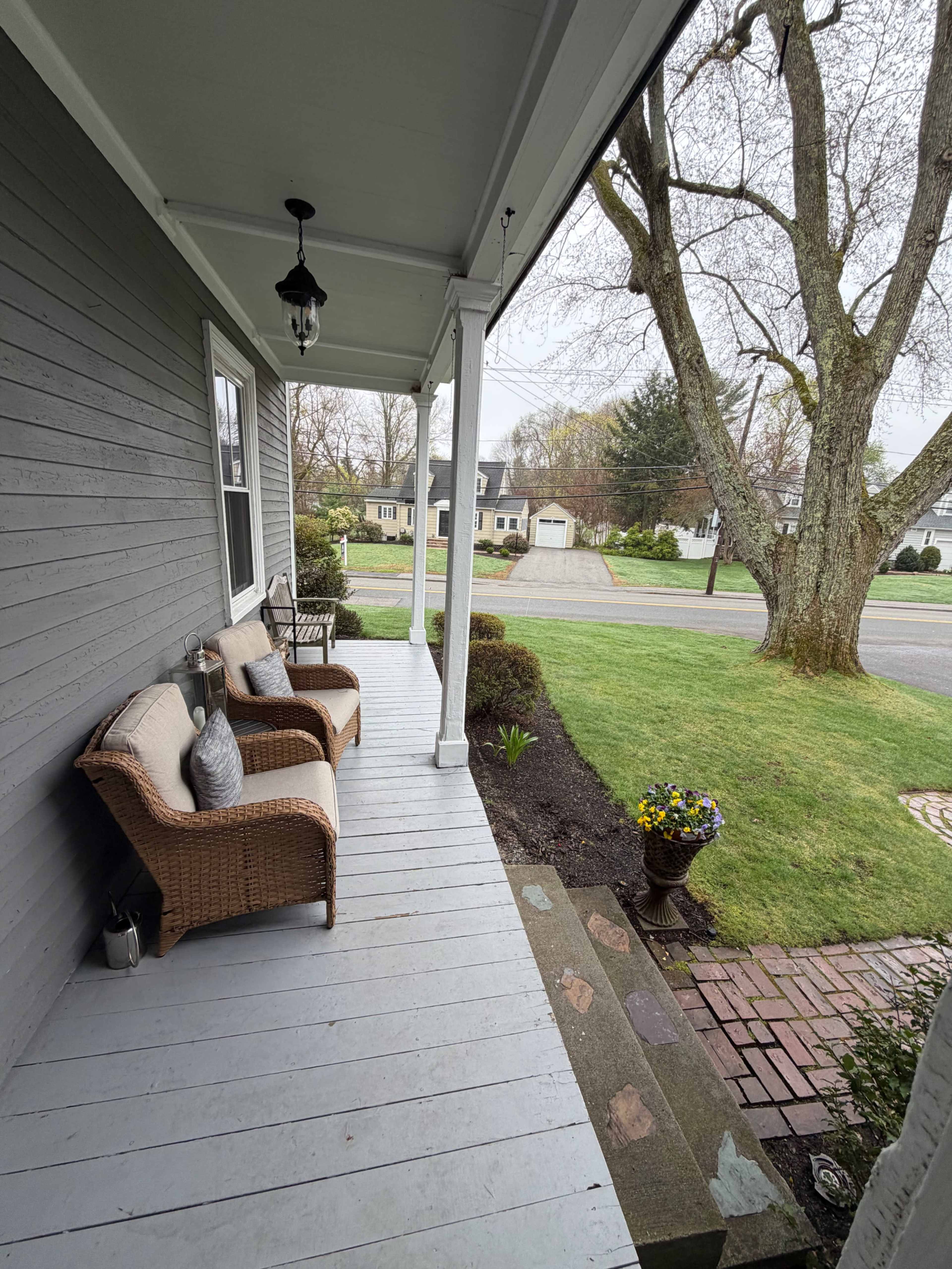 The image shows a covered porch with two wicker chairs and a view of a neighborhood street and lawn.