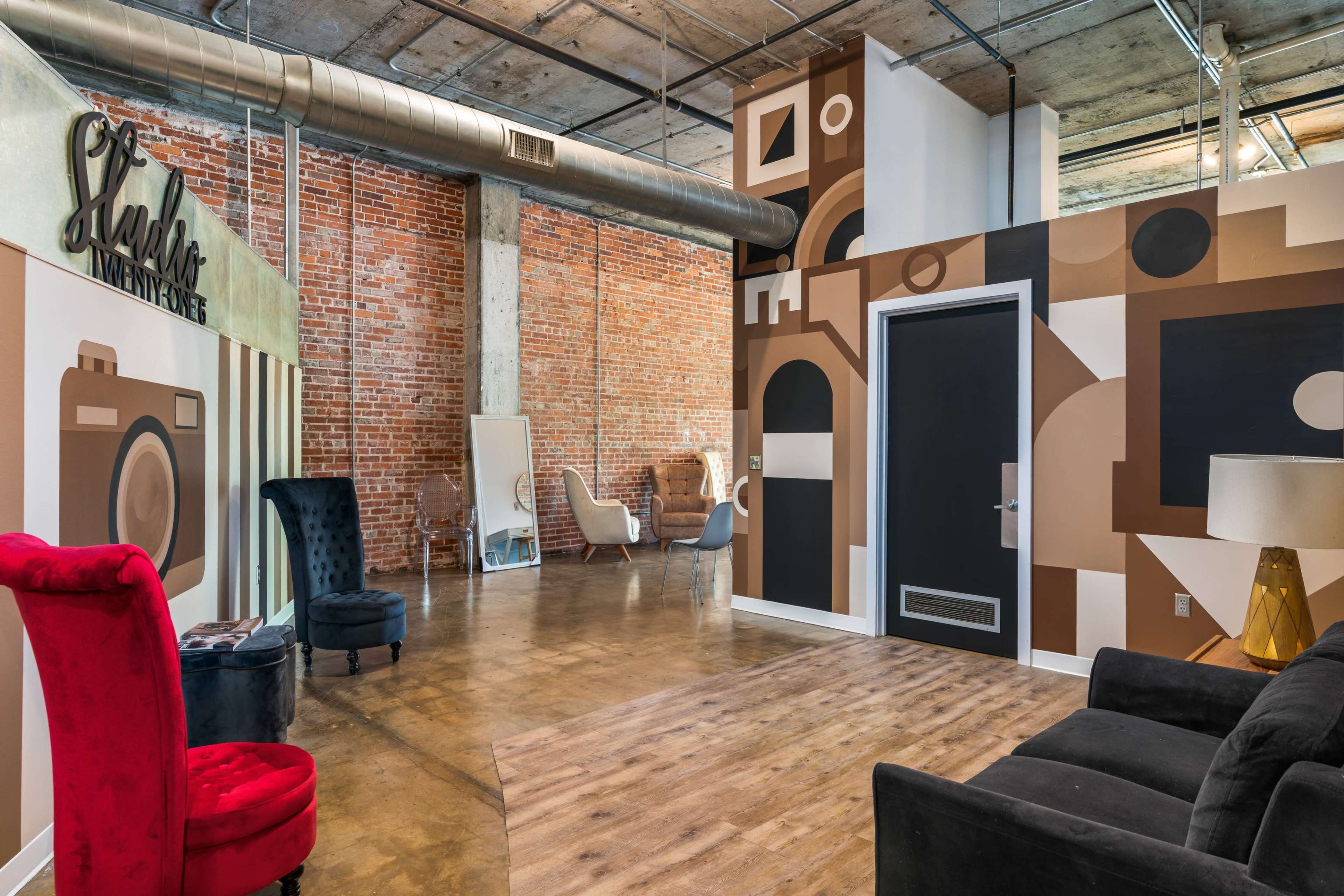 A modern interior space with exposed brick walls, artistic mural designs, and a mix of stylish furniture, including a red and a black chair.