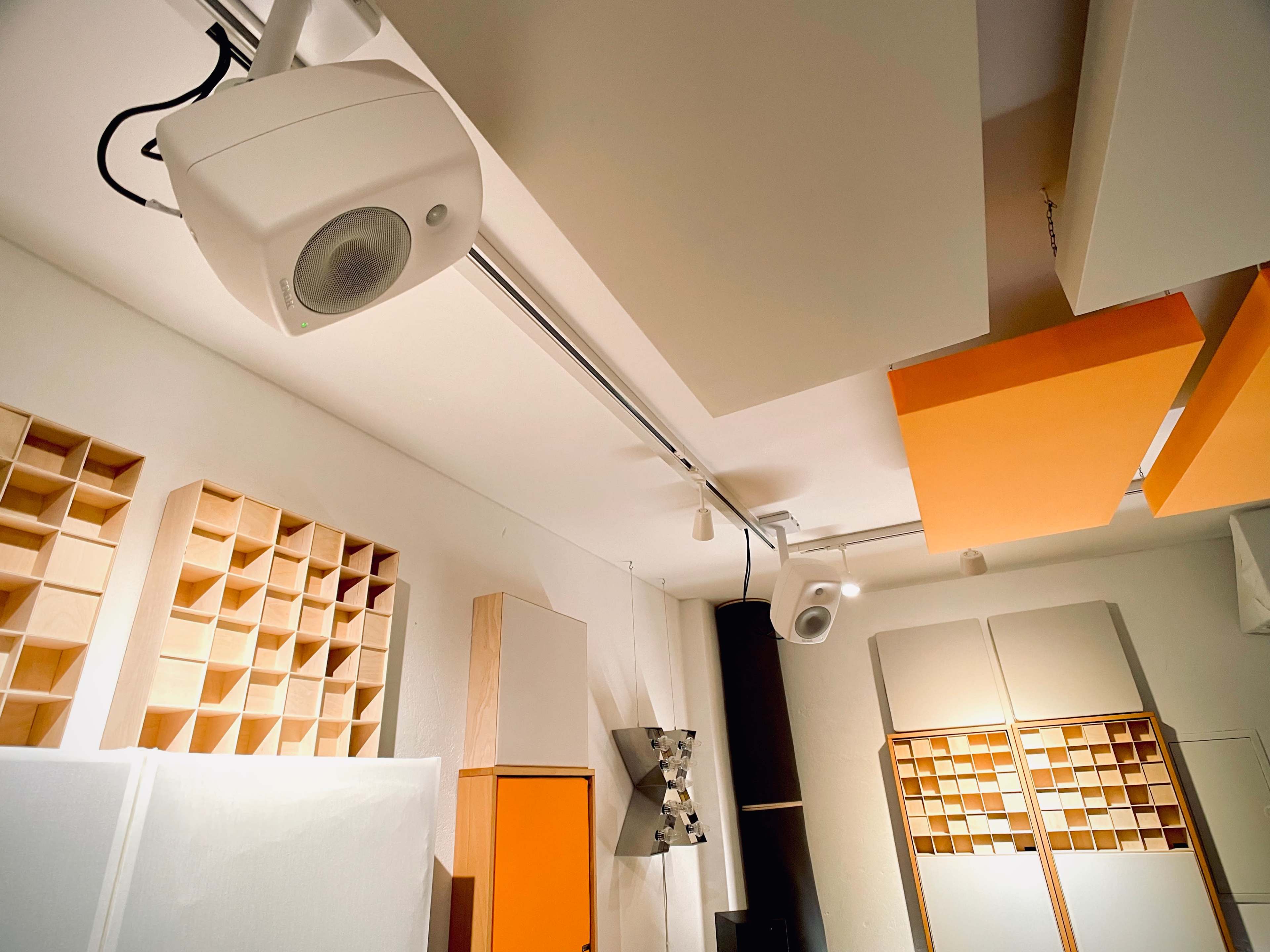 A recording studio with various acoustic panels and speakers mounted on the ceiling and walls.