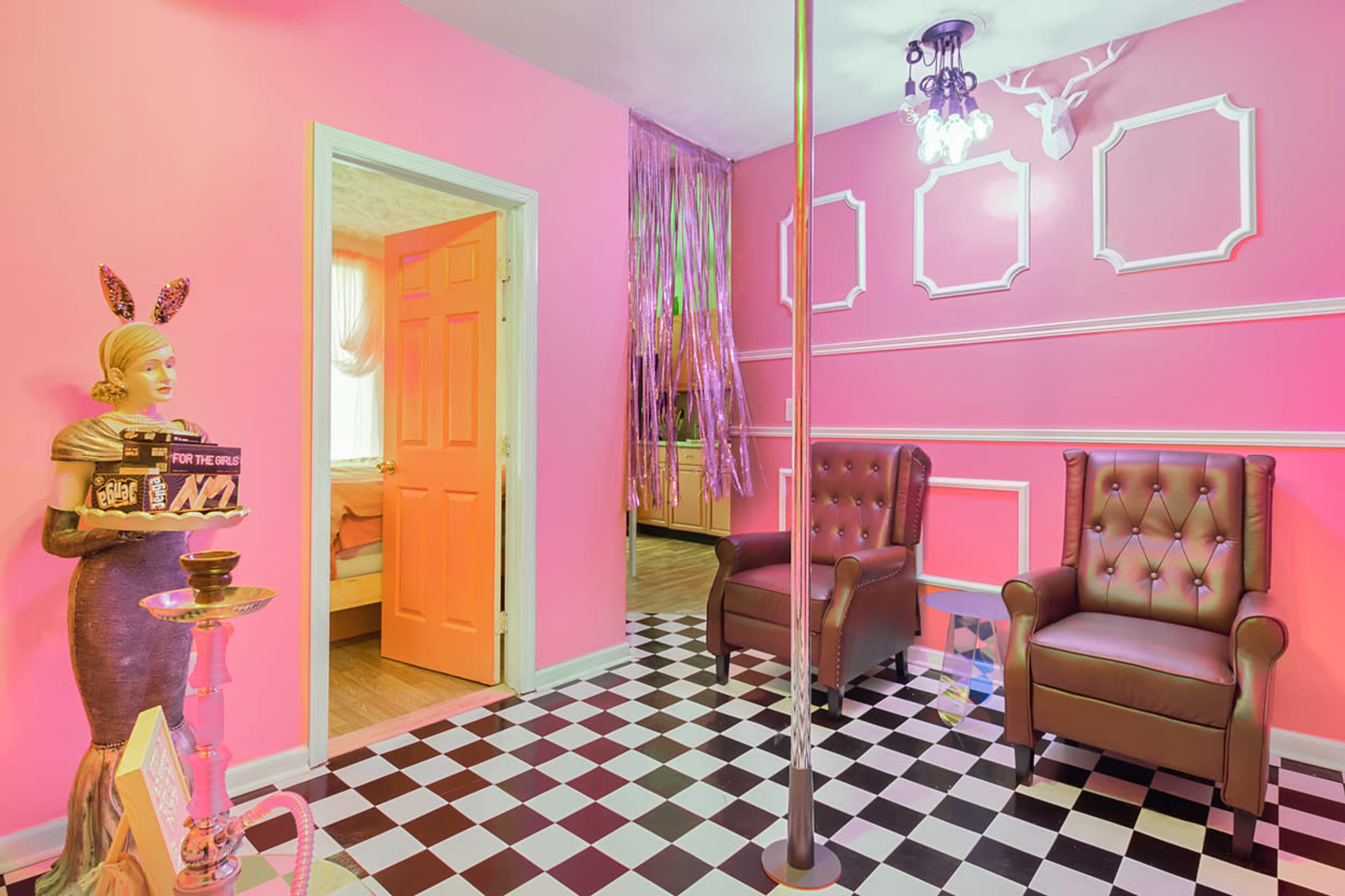 The room features pink walls, a checkered floor, two brown leather chairs, and a decorative mannequin holding a cake.