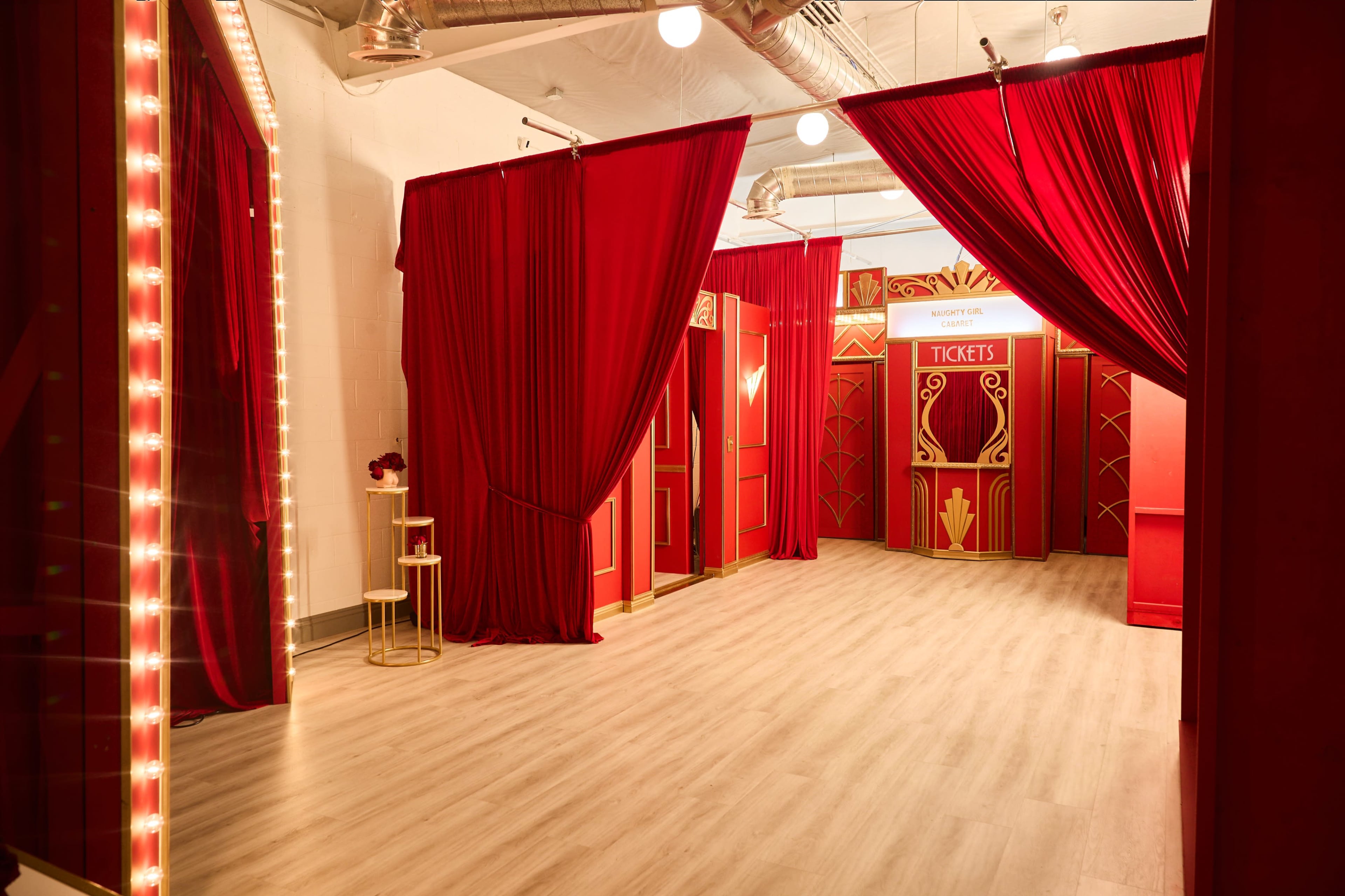 The image shows a room decorated with red curtains, vintage-style ticket booths, and a wooden floor.