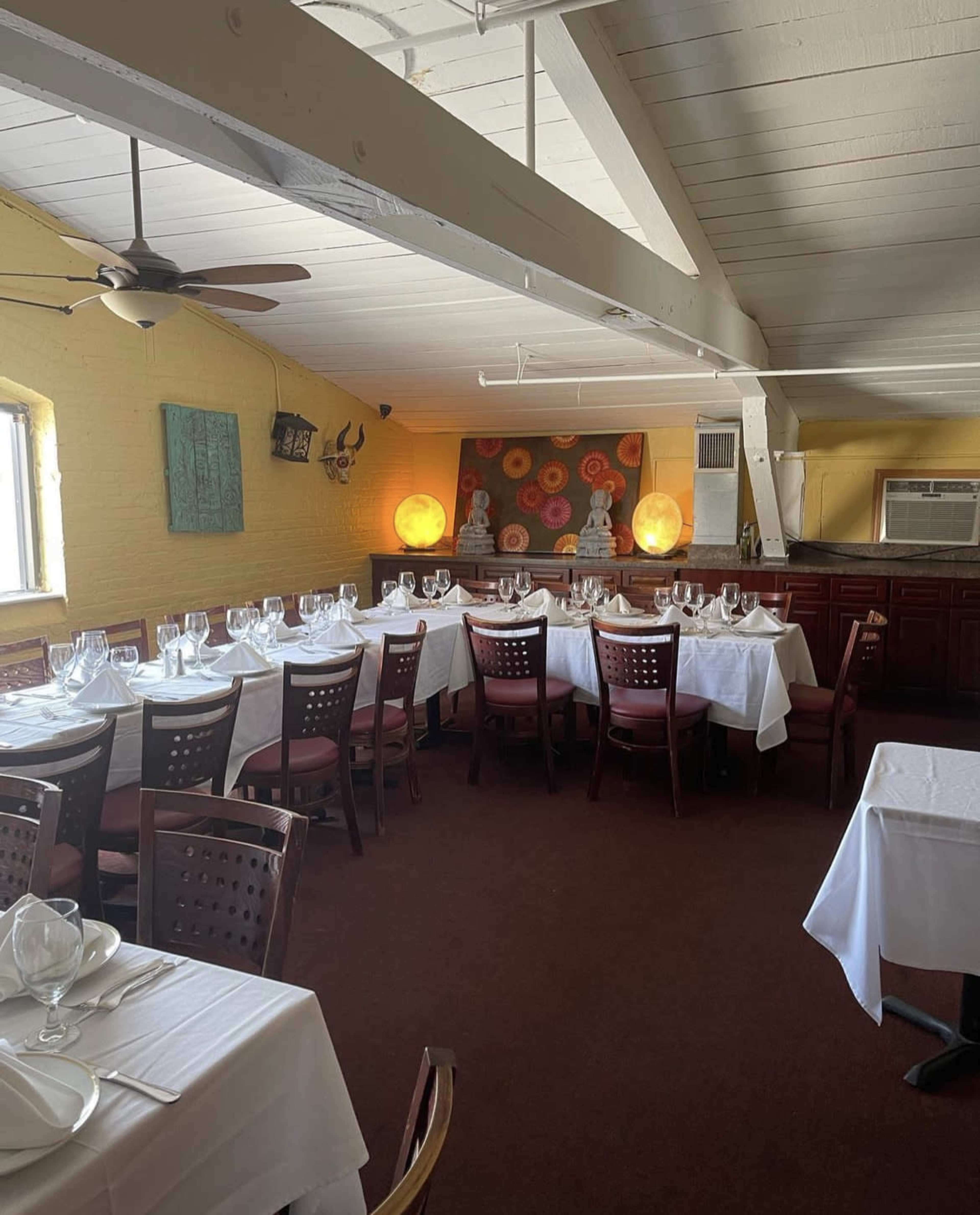 A dining area with white tablecloths and neatly arranged tables, featuring a wooden bar and colorful artwork on the walls.