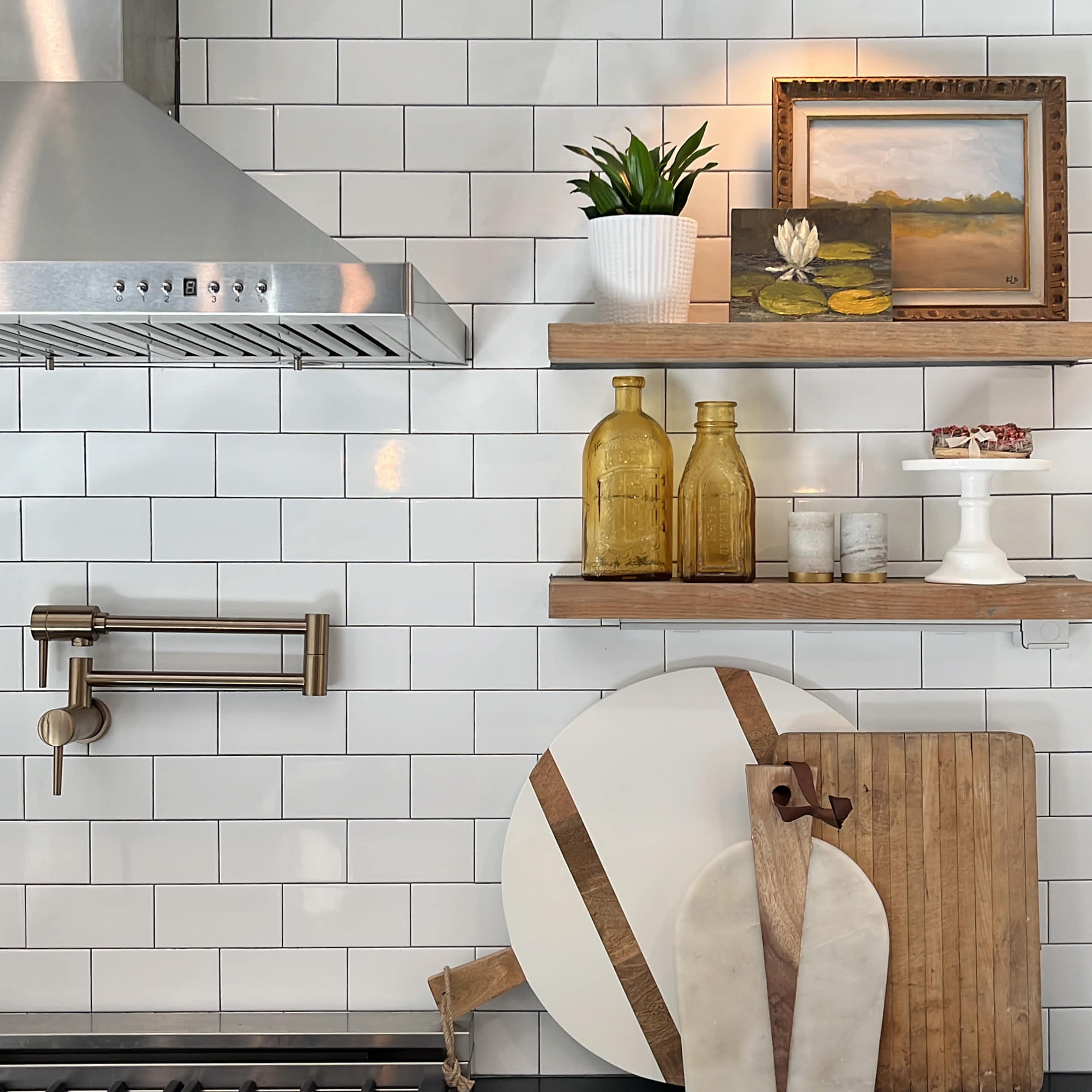 The image shows a modern kitchen with white tiled walls, featuring wooden shelves that hold decorative items, jars, and a small plant.