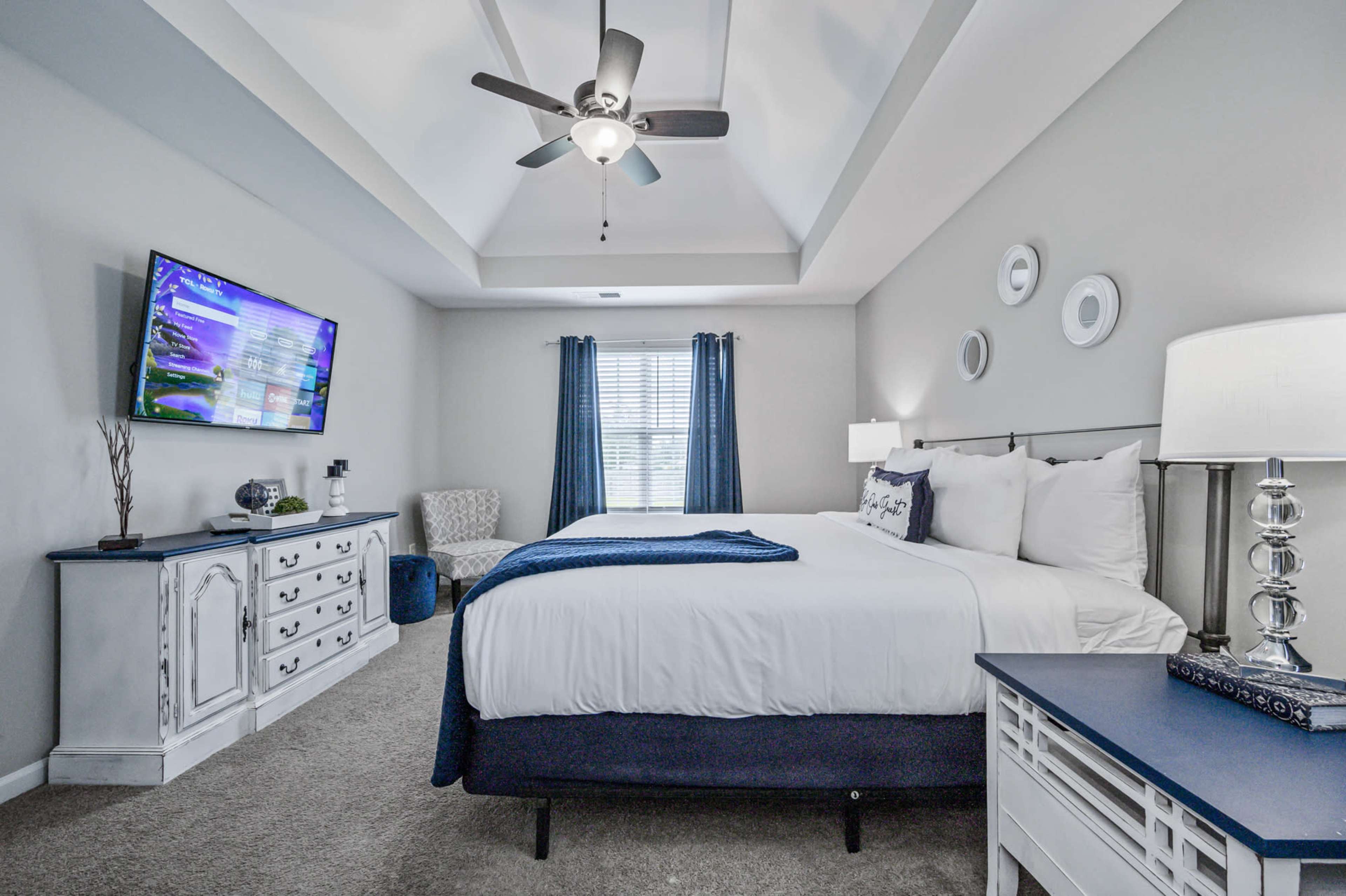 A spacious bedroom features a king-sized bed, a television mounted on the wall, and a seating area by the window.