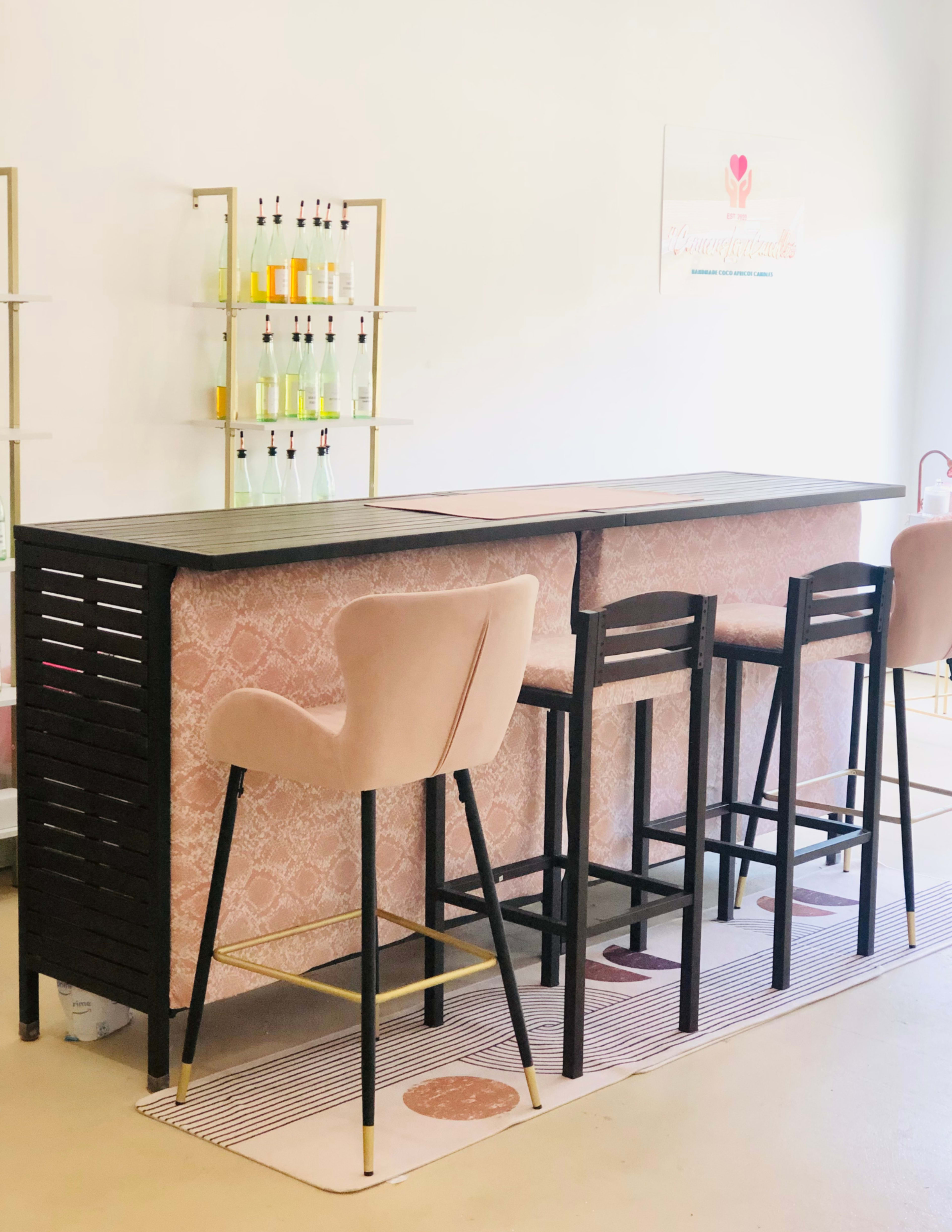 A minimalist bar setup features two types of high stools on a patterned rug, with shelves of bottles in the background.