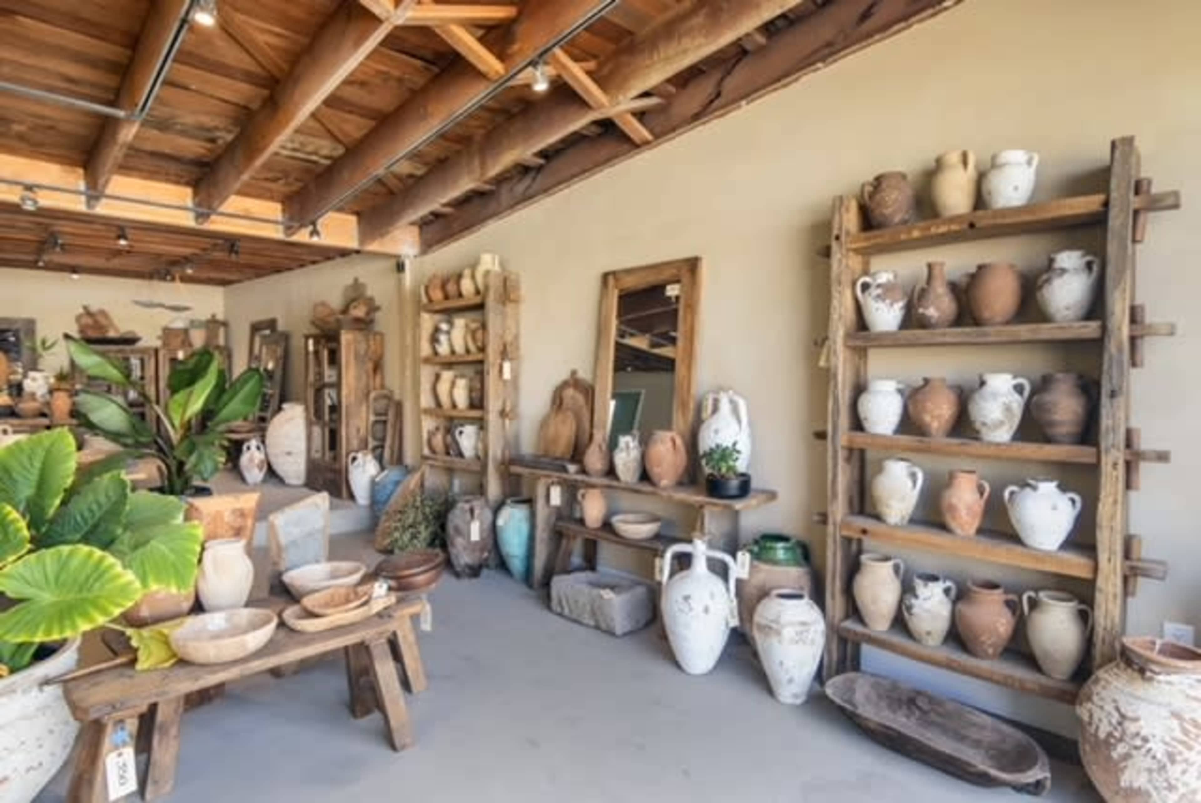 The image shows a well-organized pottery shop displaying a variety of ceramic vessels on shelves and tables, with wooden beams overhead.