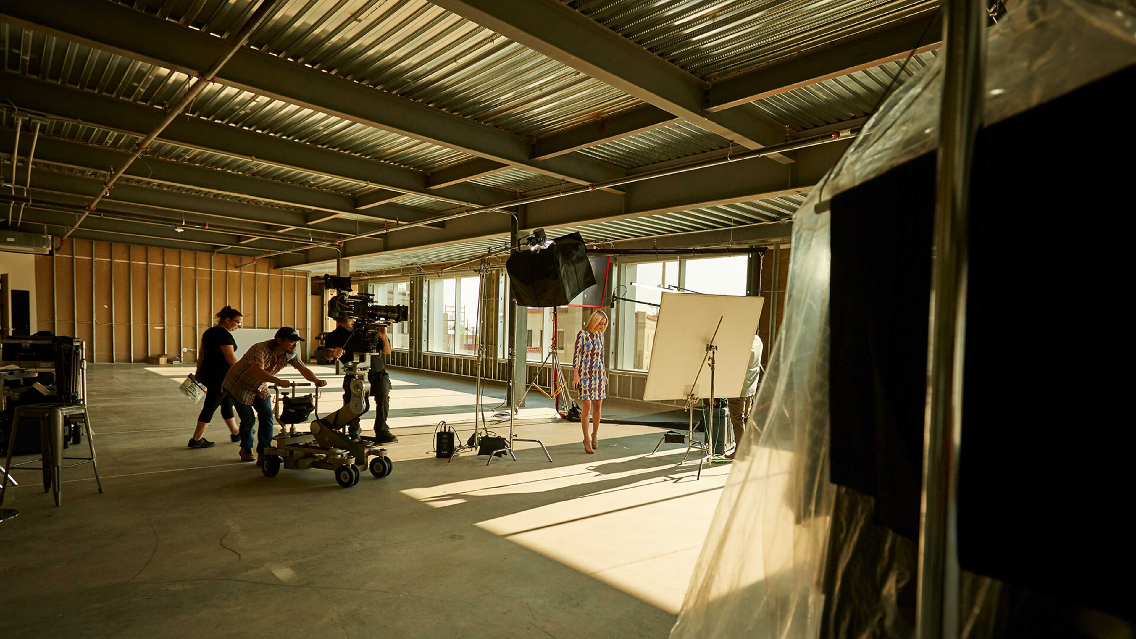 A film crew is setting up equipment in an unfinished industrial space for a photoshoot.