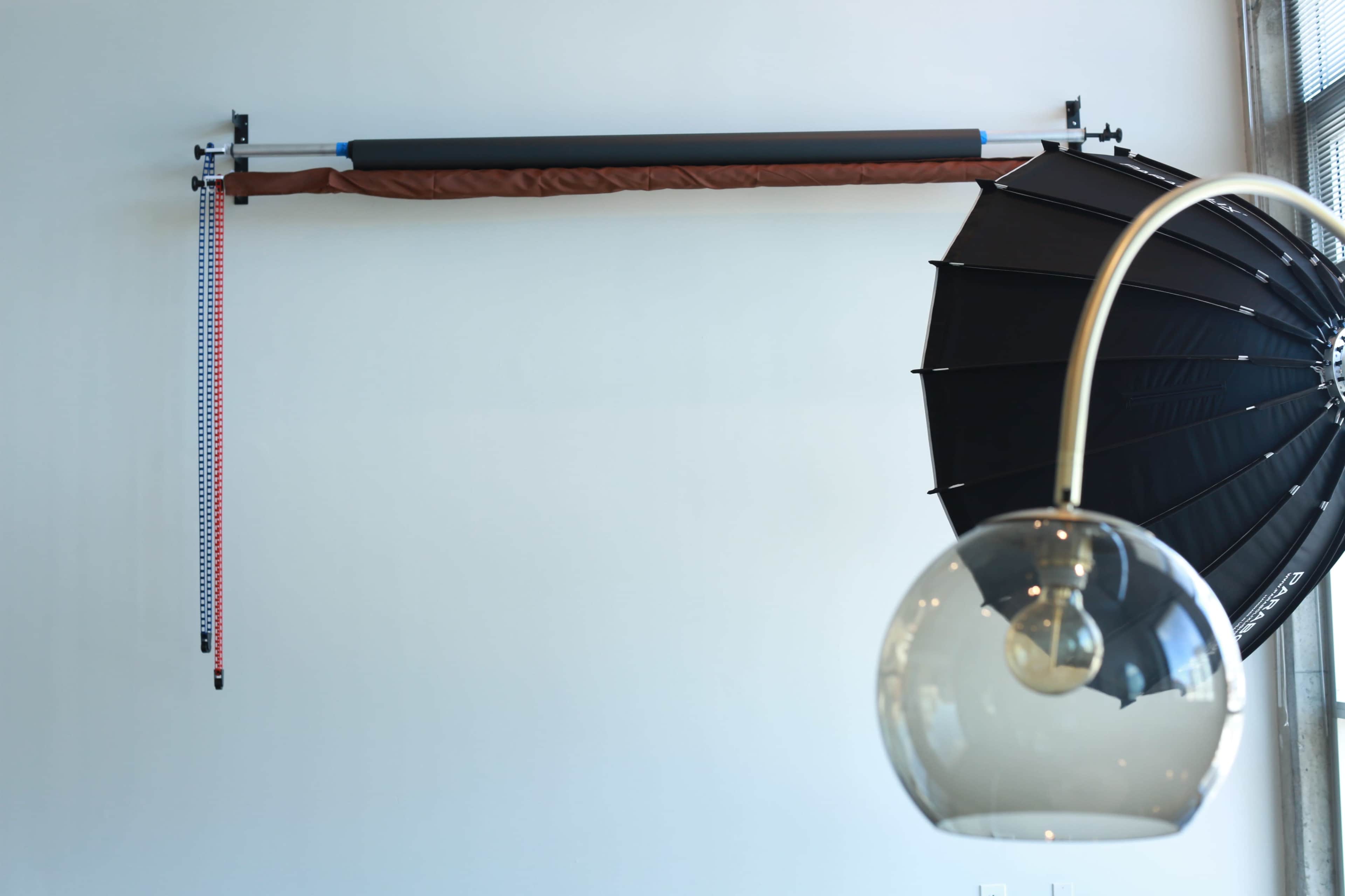 A wall-mounted backdrop support system alongside a large black umbrella light and a round pendant light.