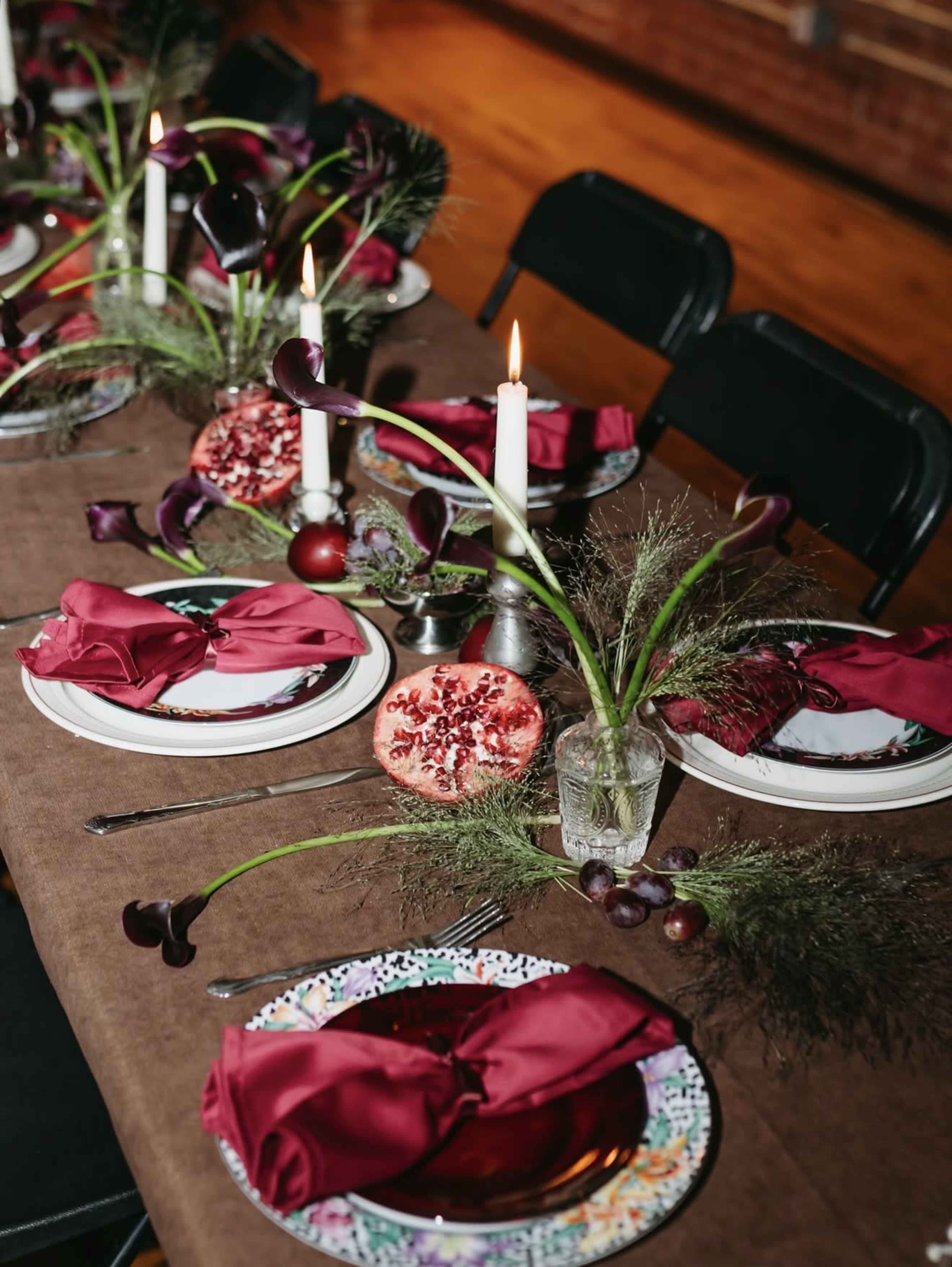 The image shows a decorated dining table set with plates, napkins, and centerpieces featuring pomegranates, candles, and floral accents.