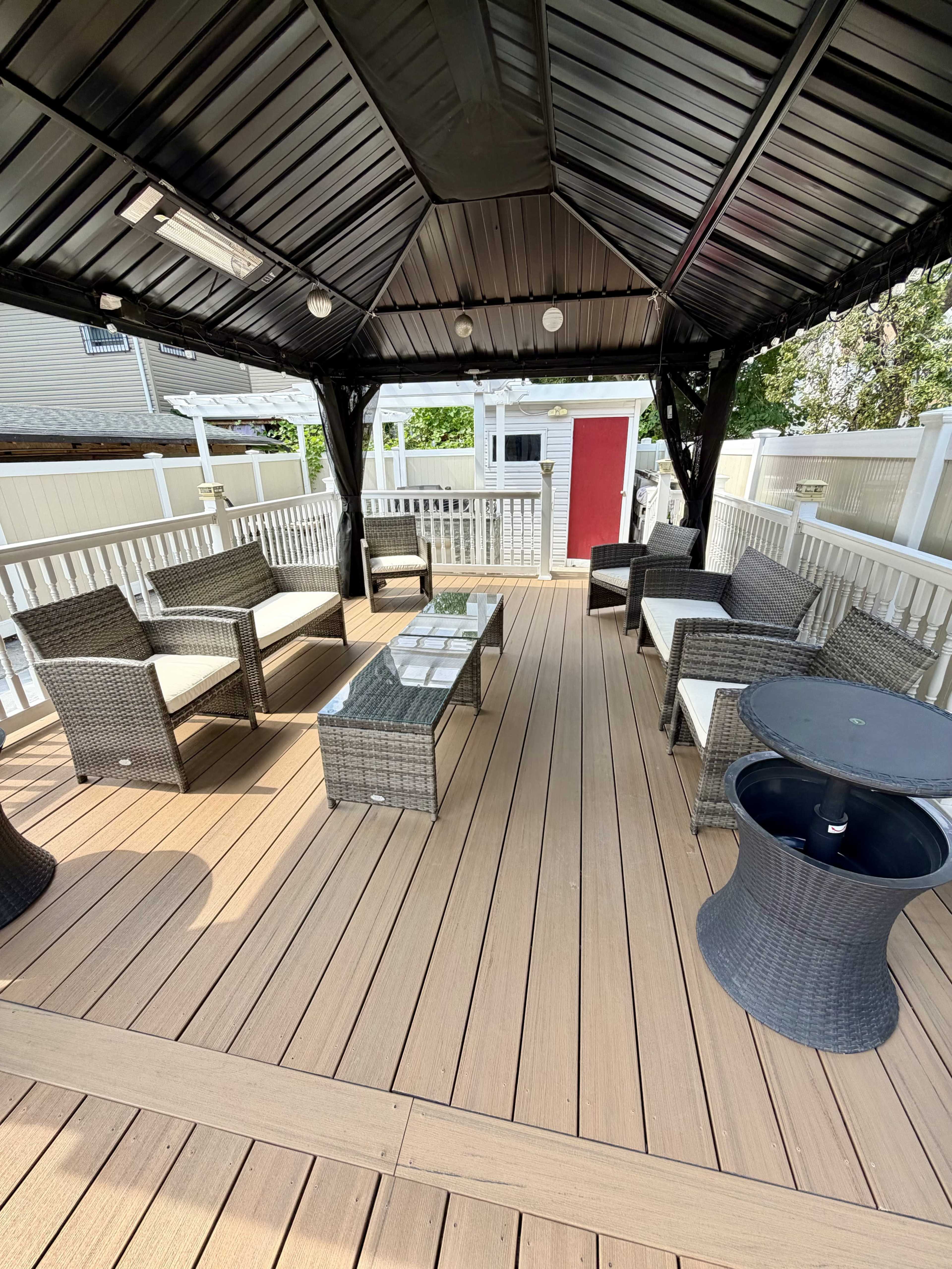 A covered outdoor seating area features wicker furniture, including chairs and tables, arranged on a wooden deck.