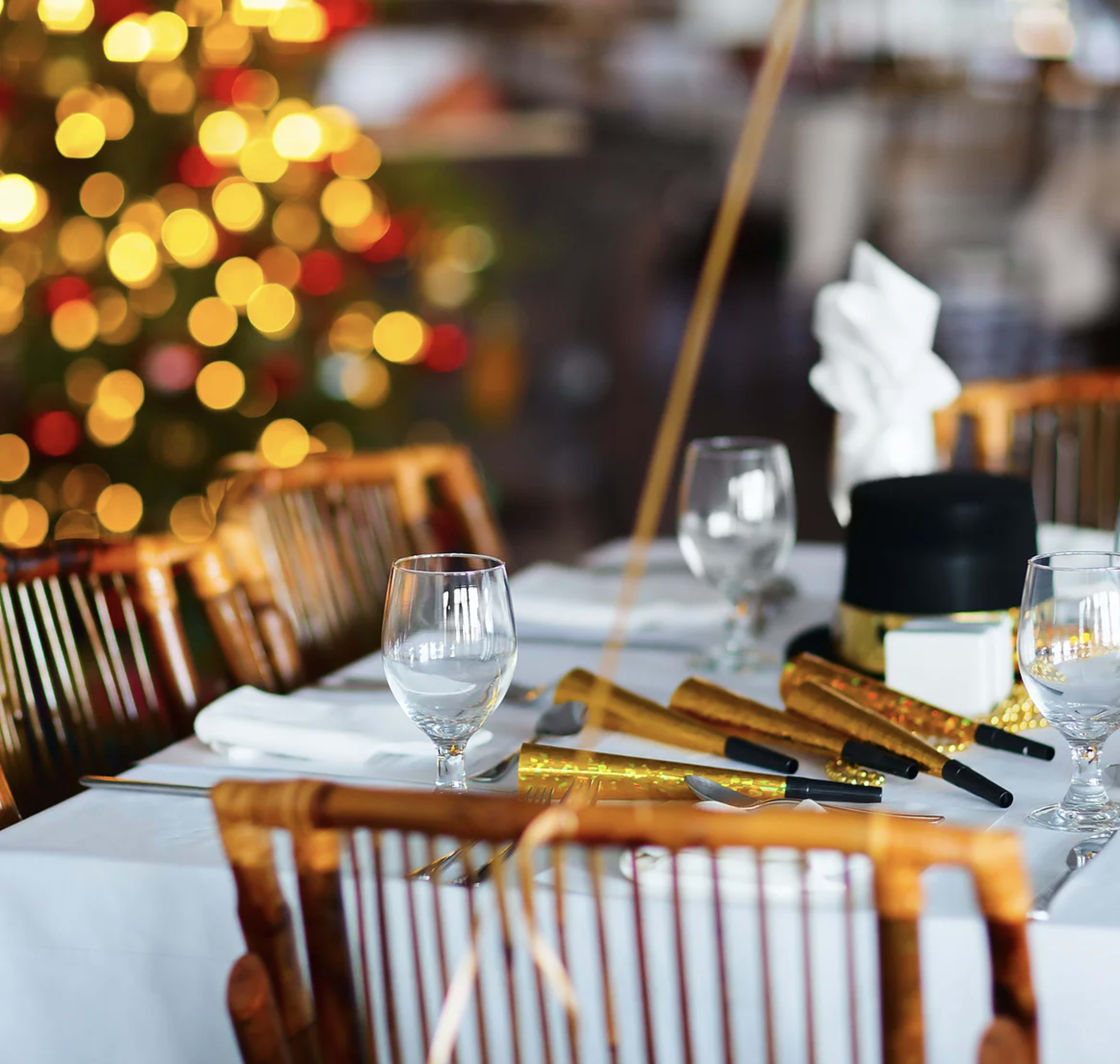 A decorated table is set with glassware and party favors, with a Christmas tree in the background.