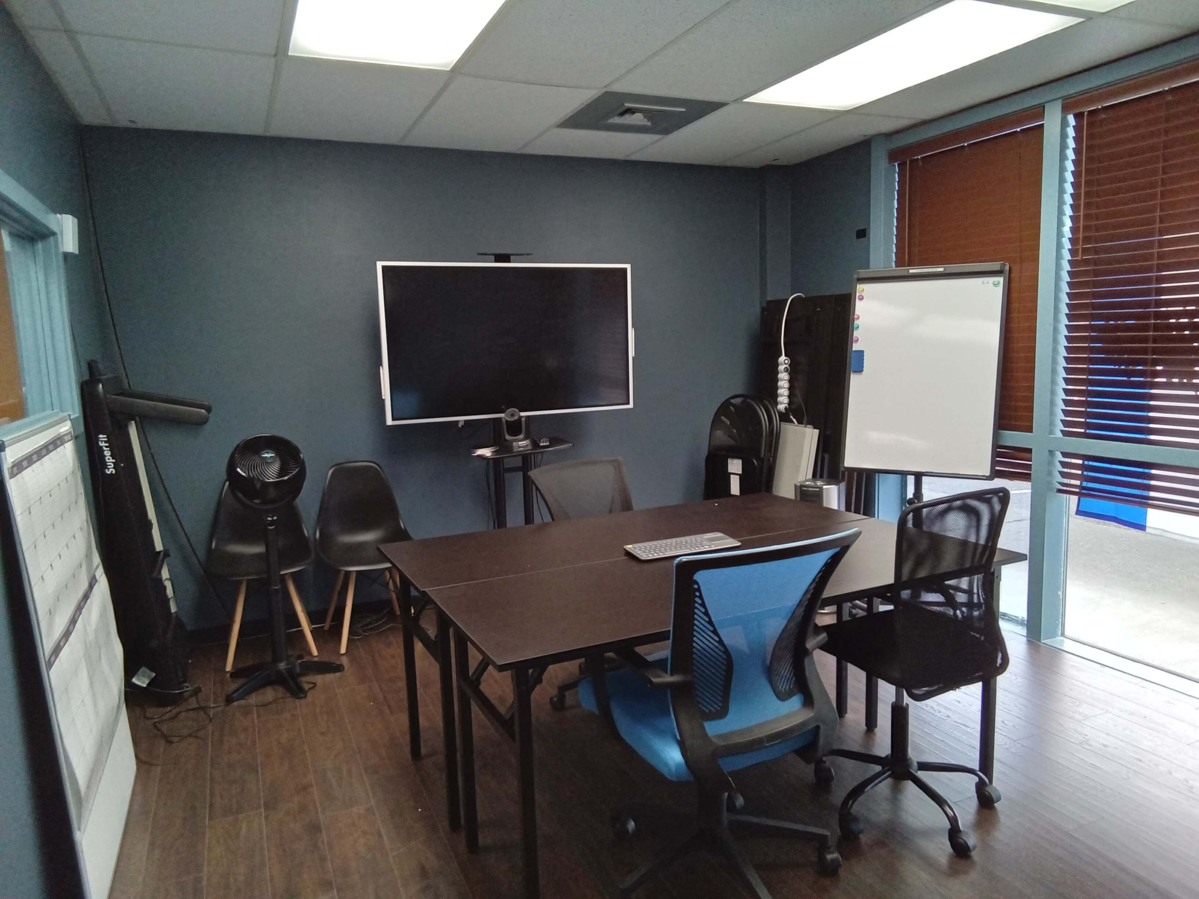 A small meeting room features a table with chairs, a large monitor on the wall, and a whiteboard.
