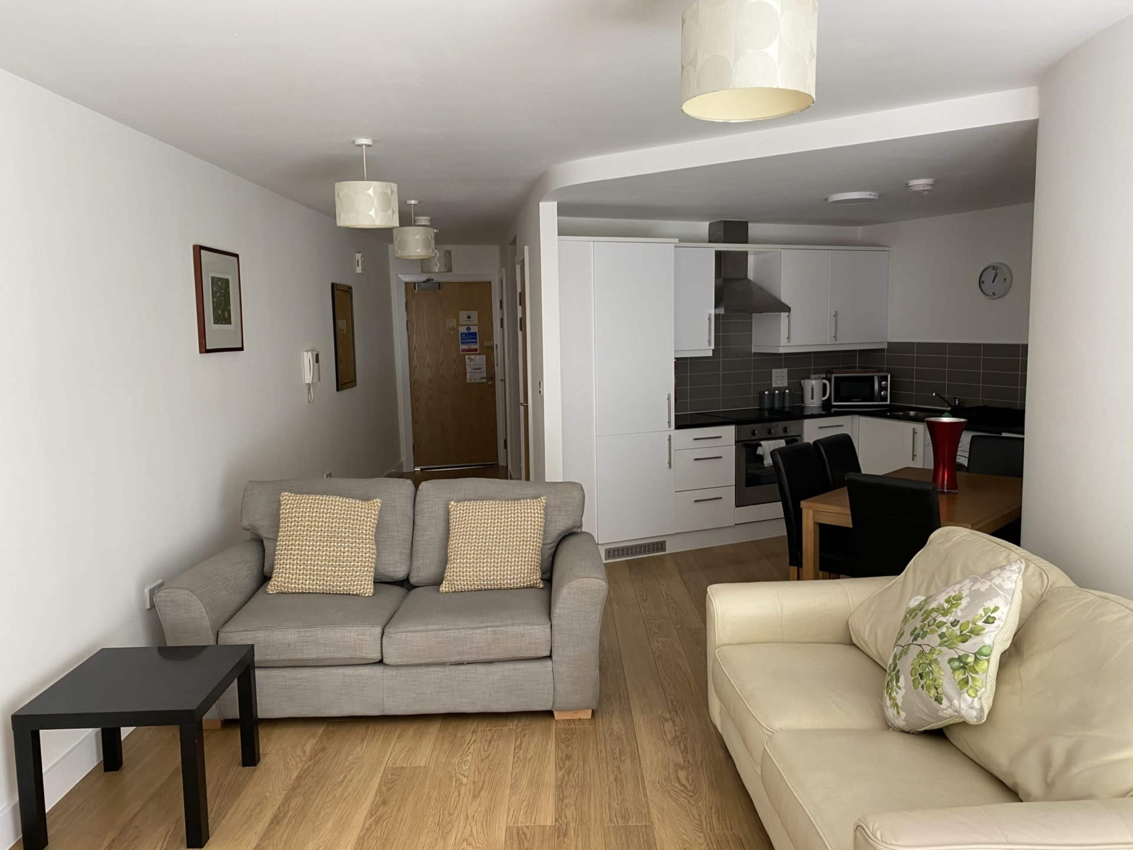 A modern living area with two sofas, a coffee table, and a small dining table next to a kitchenette.