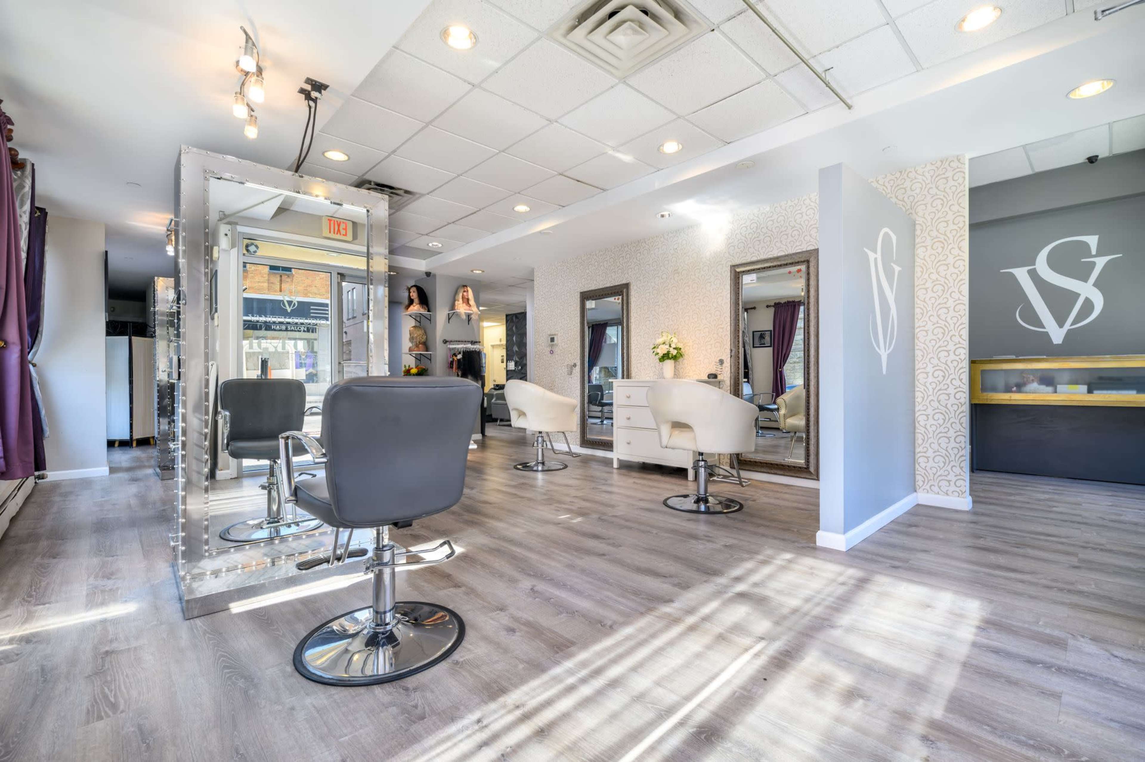 A modern hair salon with several styling stations, mirrors, and a reception area.