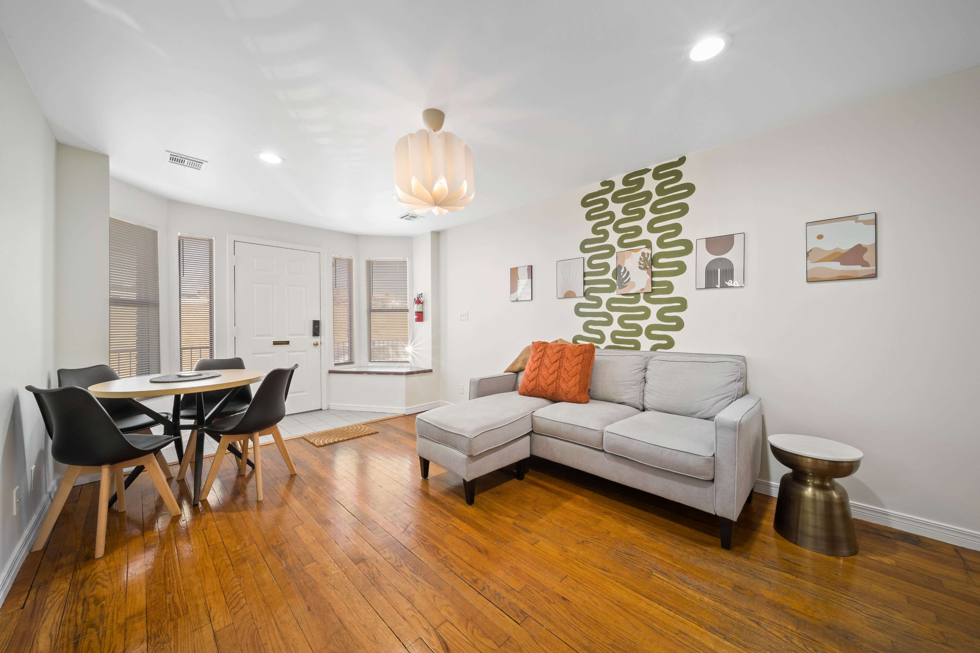 The image shows a modern living room with a sectional sofa, a circular dining table, and decorative wall art, all featuring hardwood flooring.