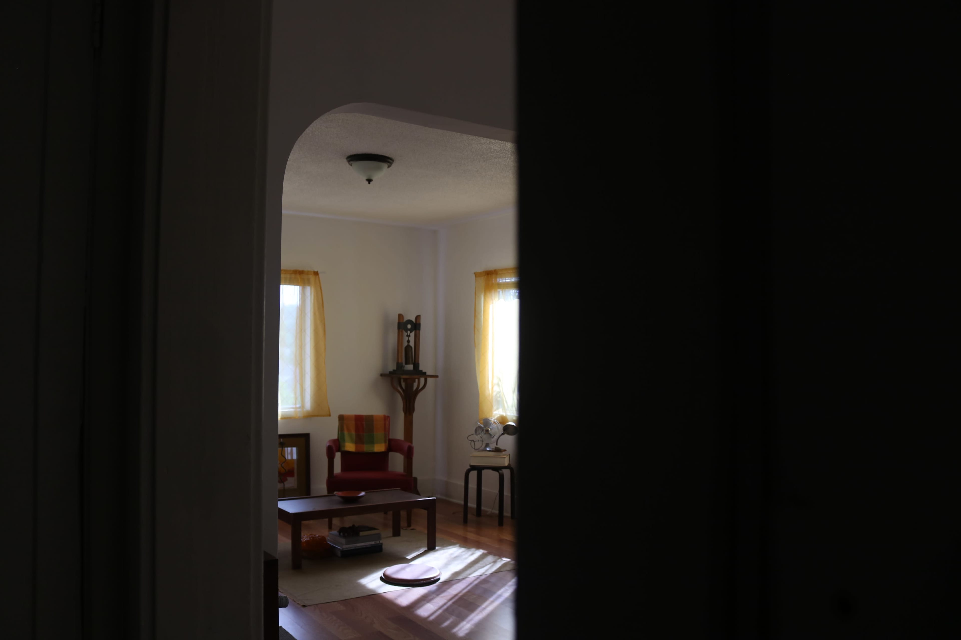 A partially open door reveals a bright living room with a red chair, a coffee table, and two windows with yellow curtains.