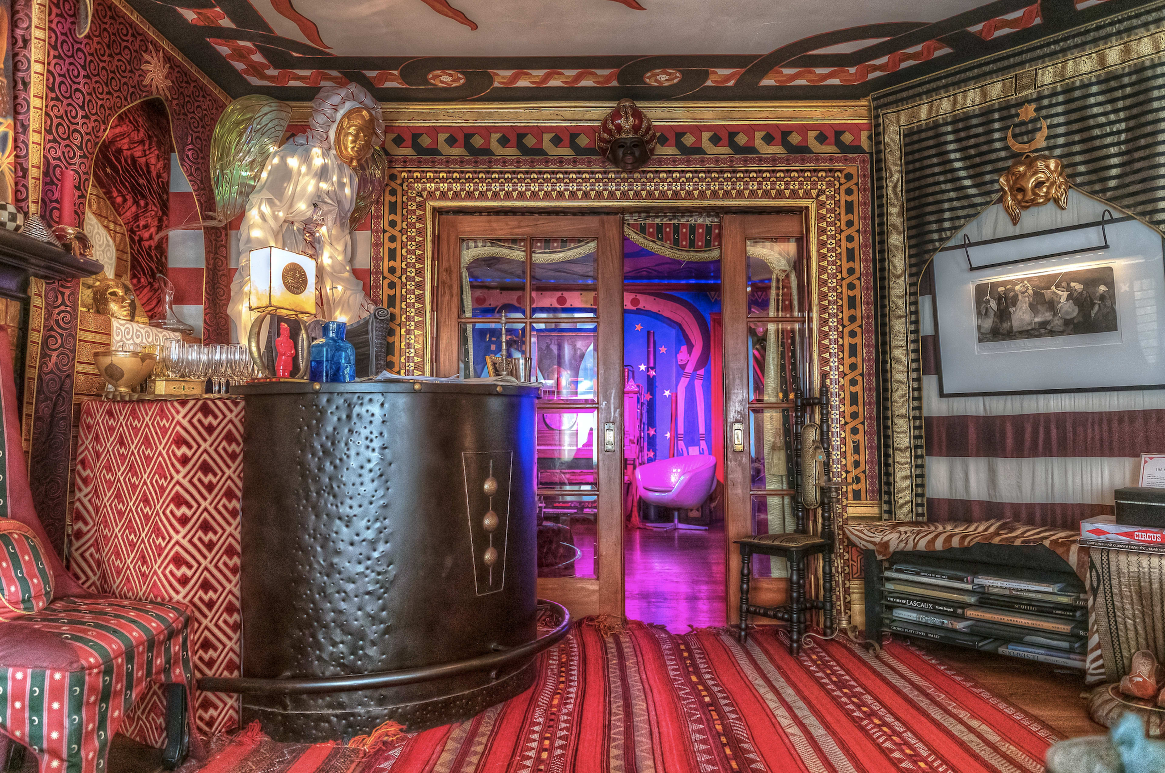 A colorful and intricately decorated interior space, featuring a curved bar, patterned walls, and a visible entrance to a room lit with vibrant purple hues.