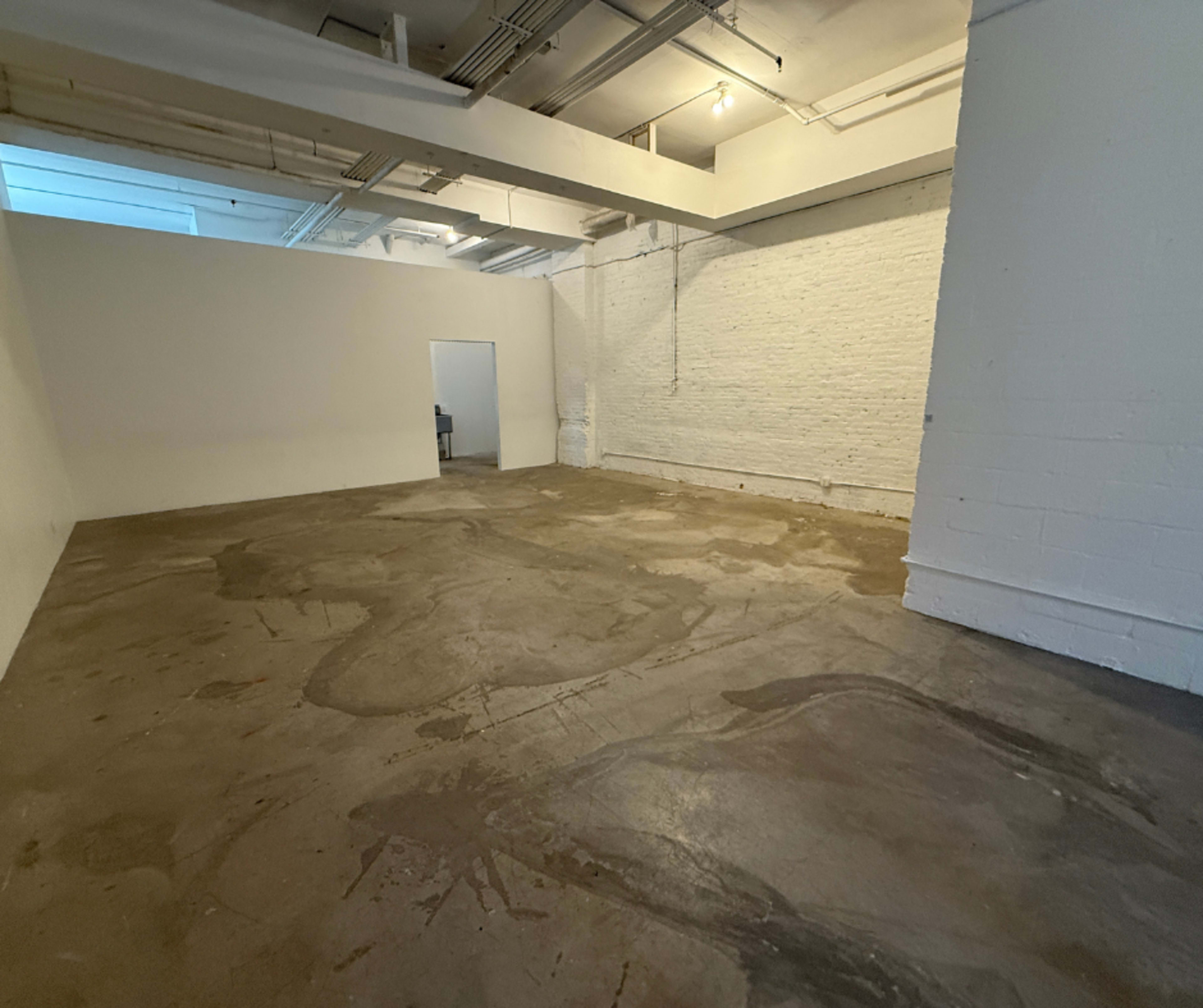 The image shows a spacious, empty interior room with bare concrete floors and white walls.