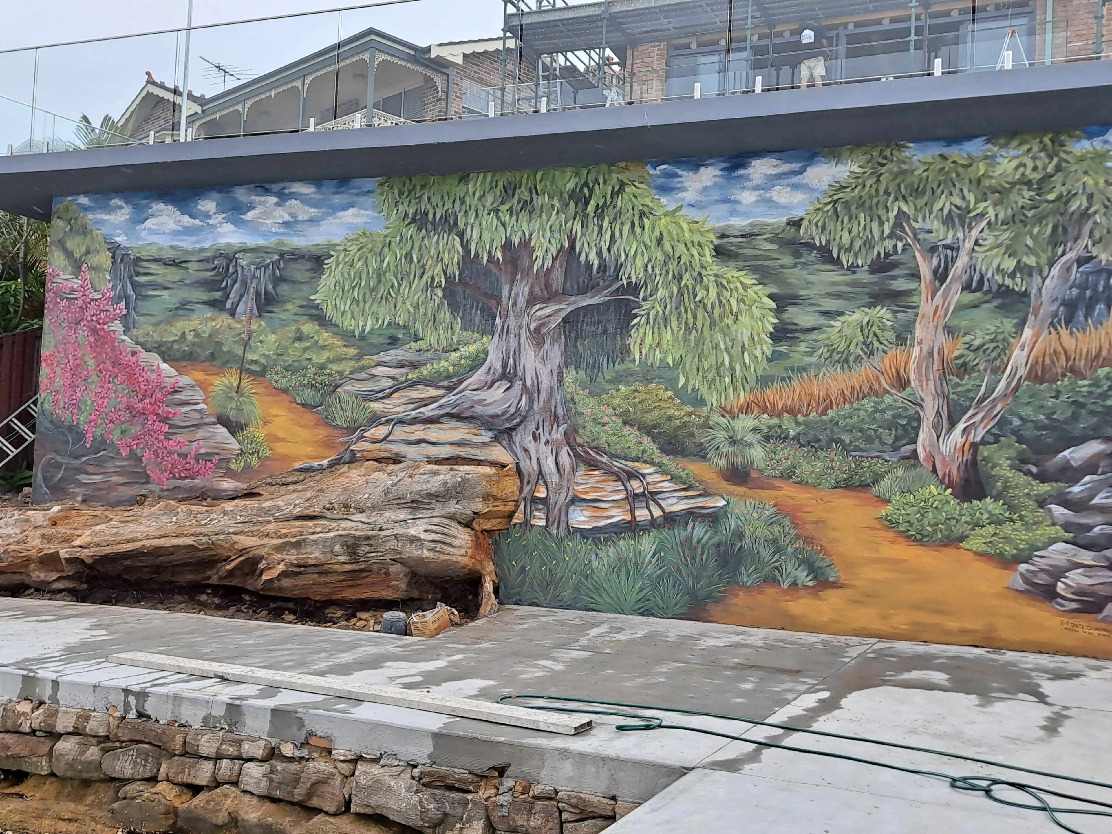 The image features a large mural depicting a scenic landscape with a winding path bordered by trees and colorful vegetation.