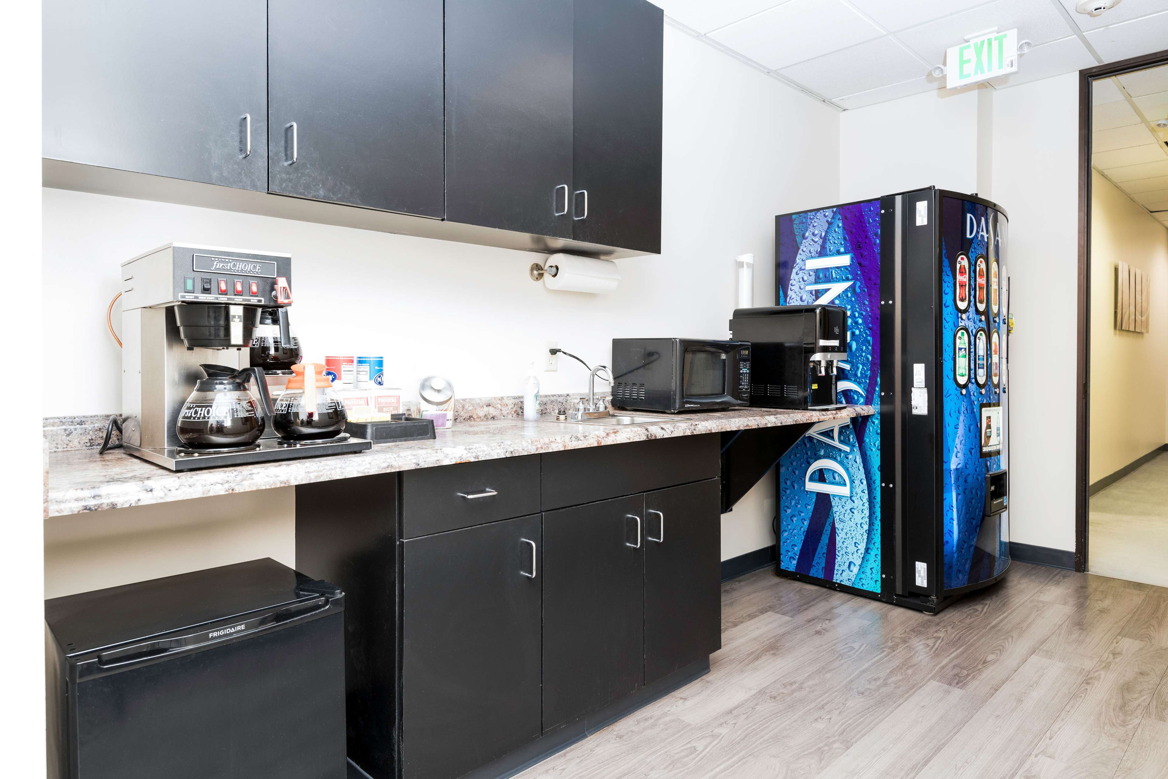 A kitchenette with a coffee maker, two microwaves, a small refrigerator, and a vending machine along a countertop.