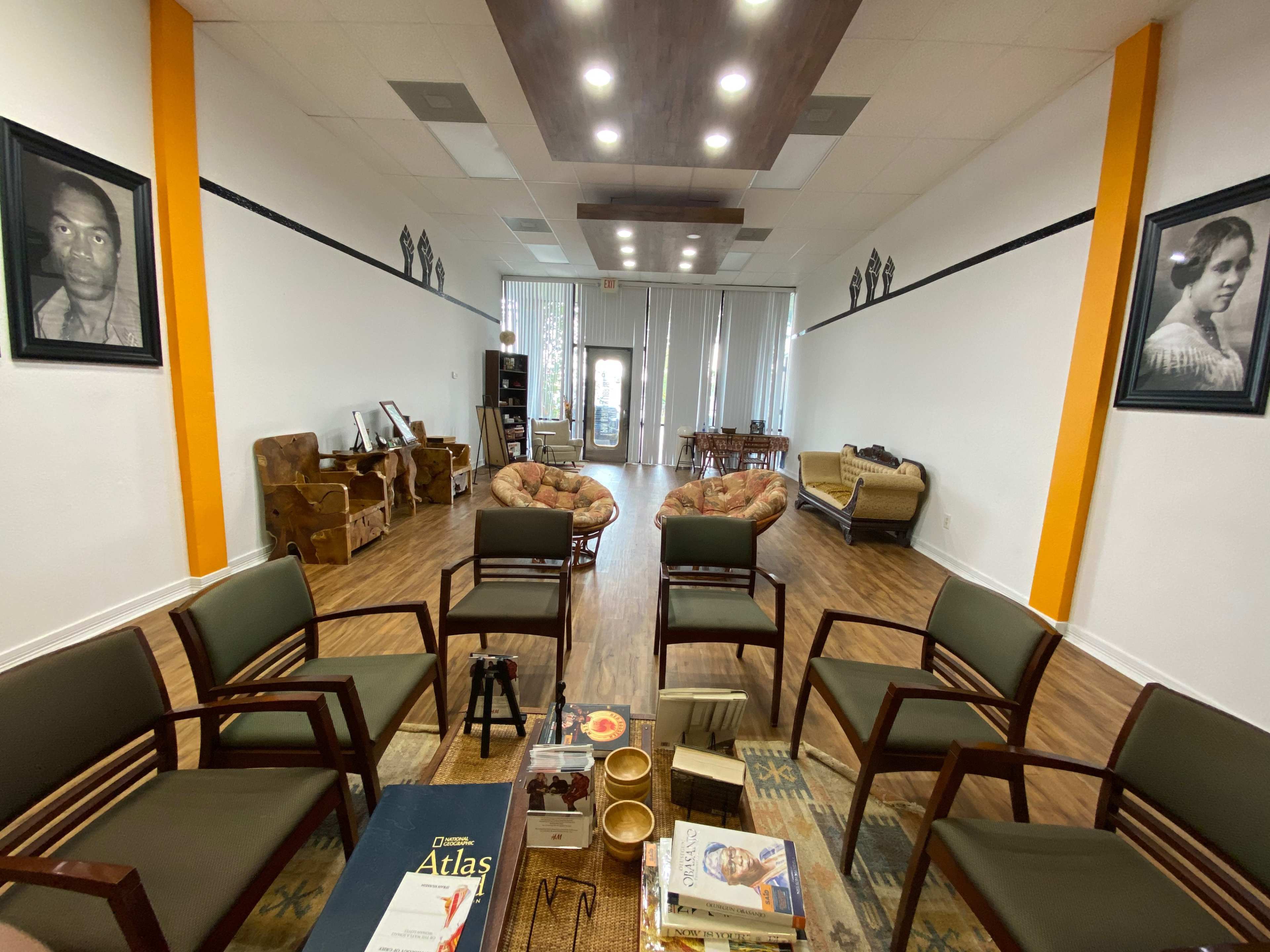 A spacious waiting area with several chairs arranged around a coffee table, framed portraits on the walls, and various seating options along the sides.