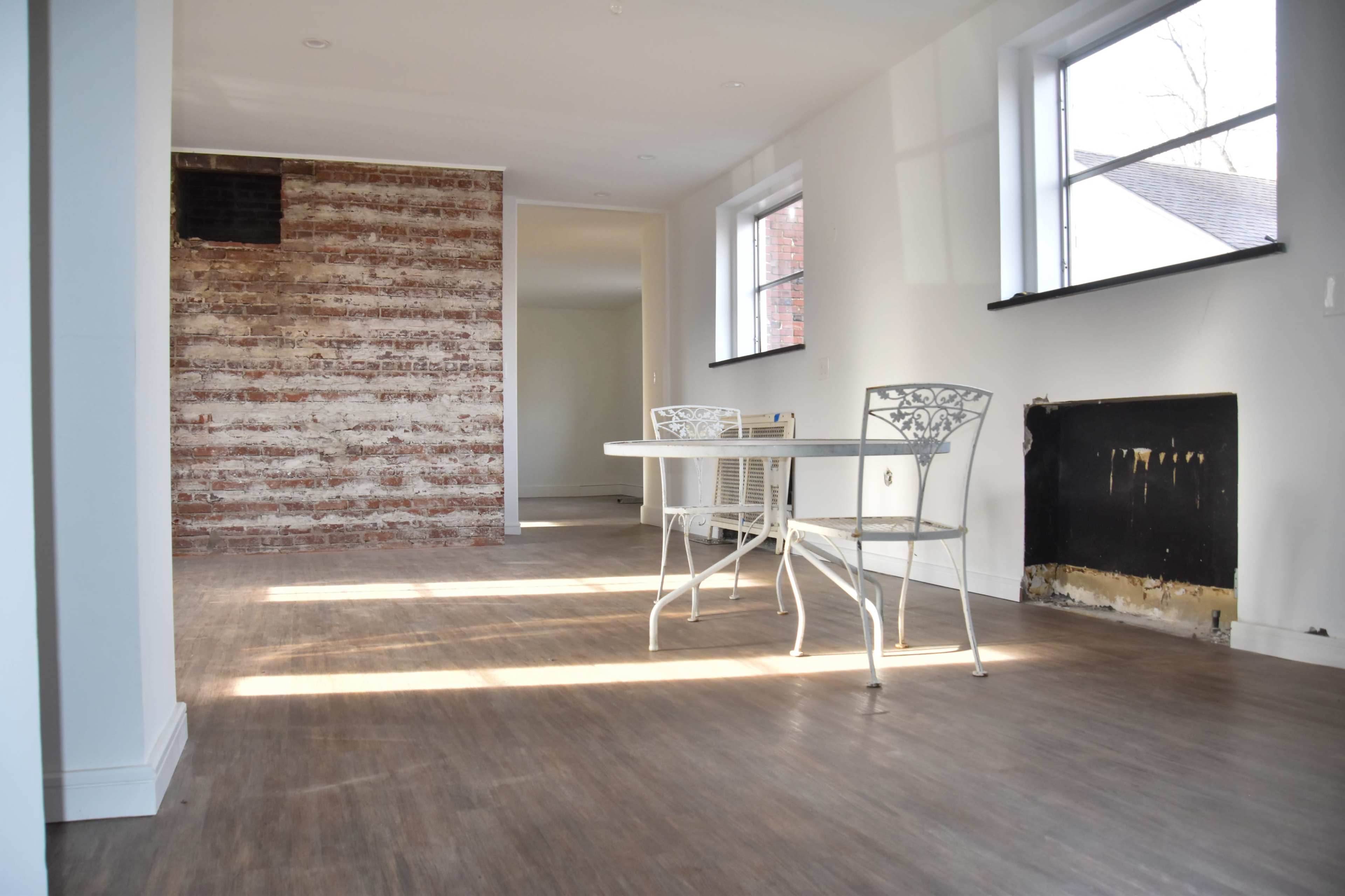 A spacious, unfinished room with a brick accent wall, two metal chairs, and a round table.
