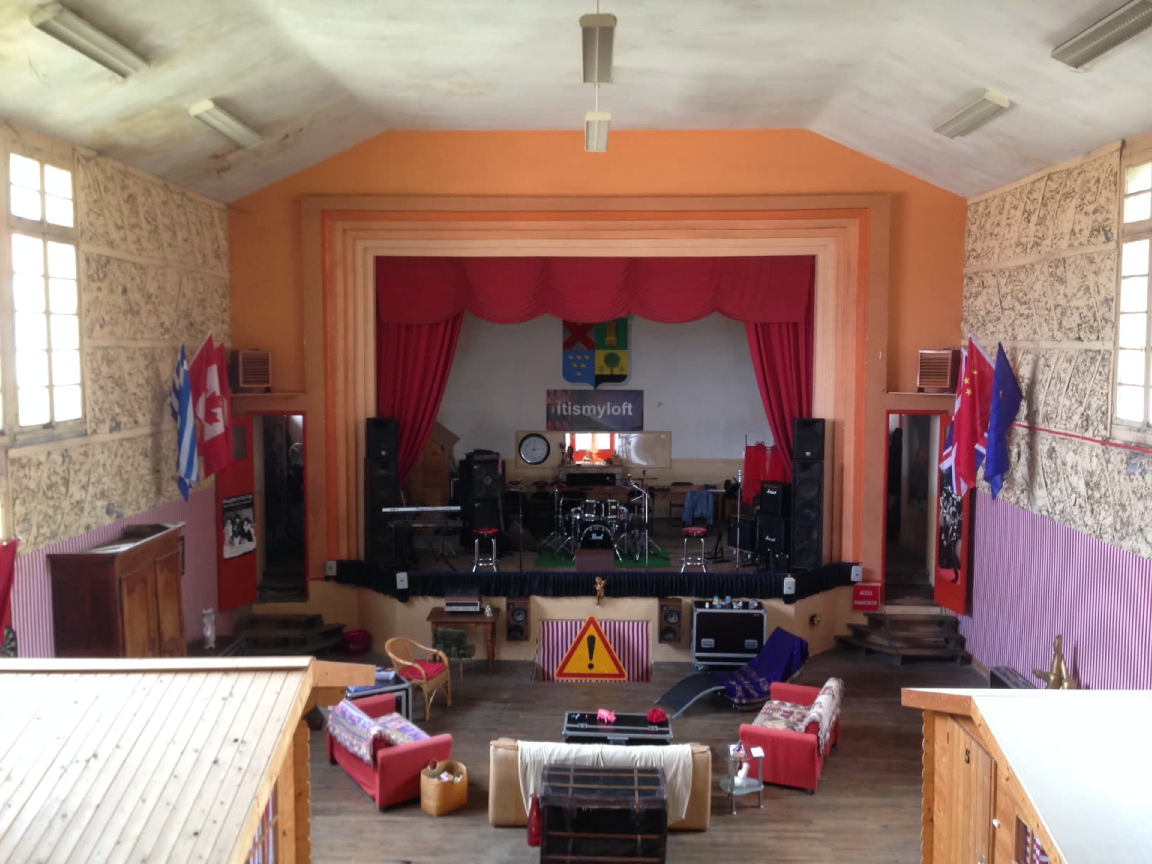 A spacious performance venue with a stage, sound equipment, and seating arrangements, adorned with colorful banners and flags.