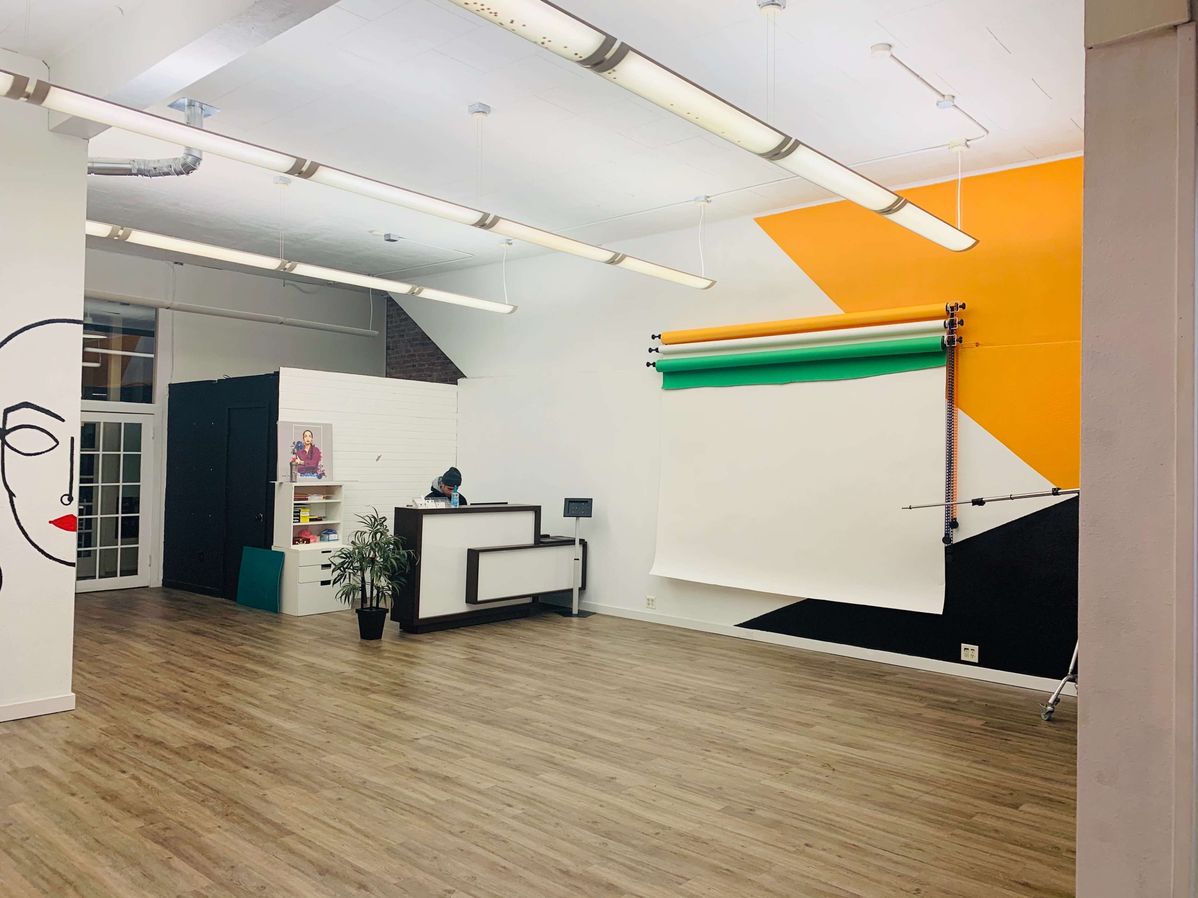 The interior of a photography studio features a reception area, colorful accent walls, and a roll of backdrop paper.