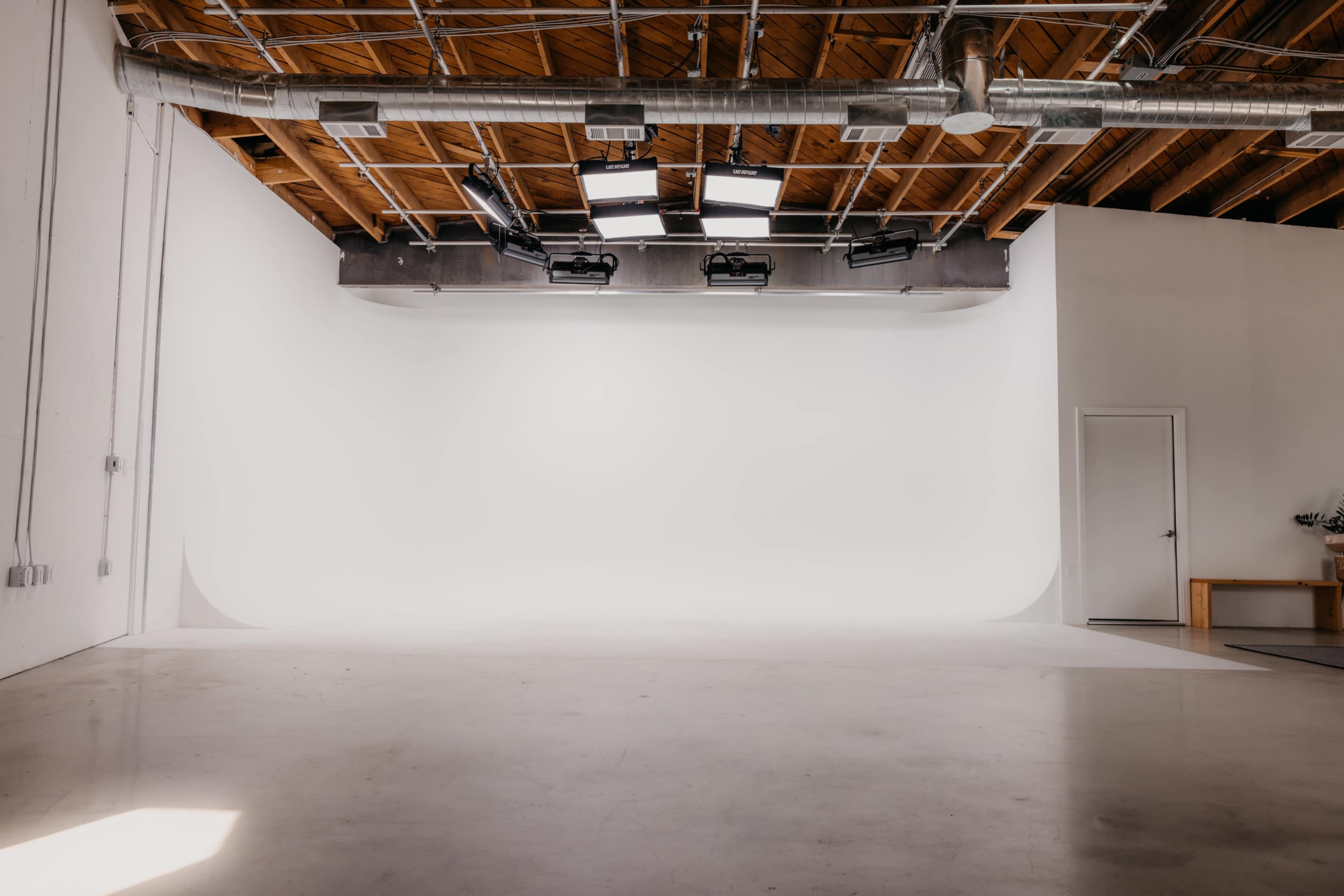 The image features an empty studio space with a seamless white backdrop and overhead lighting.