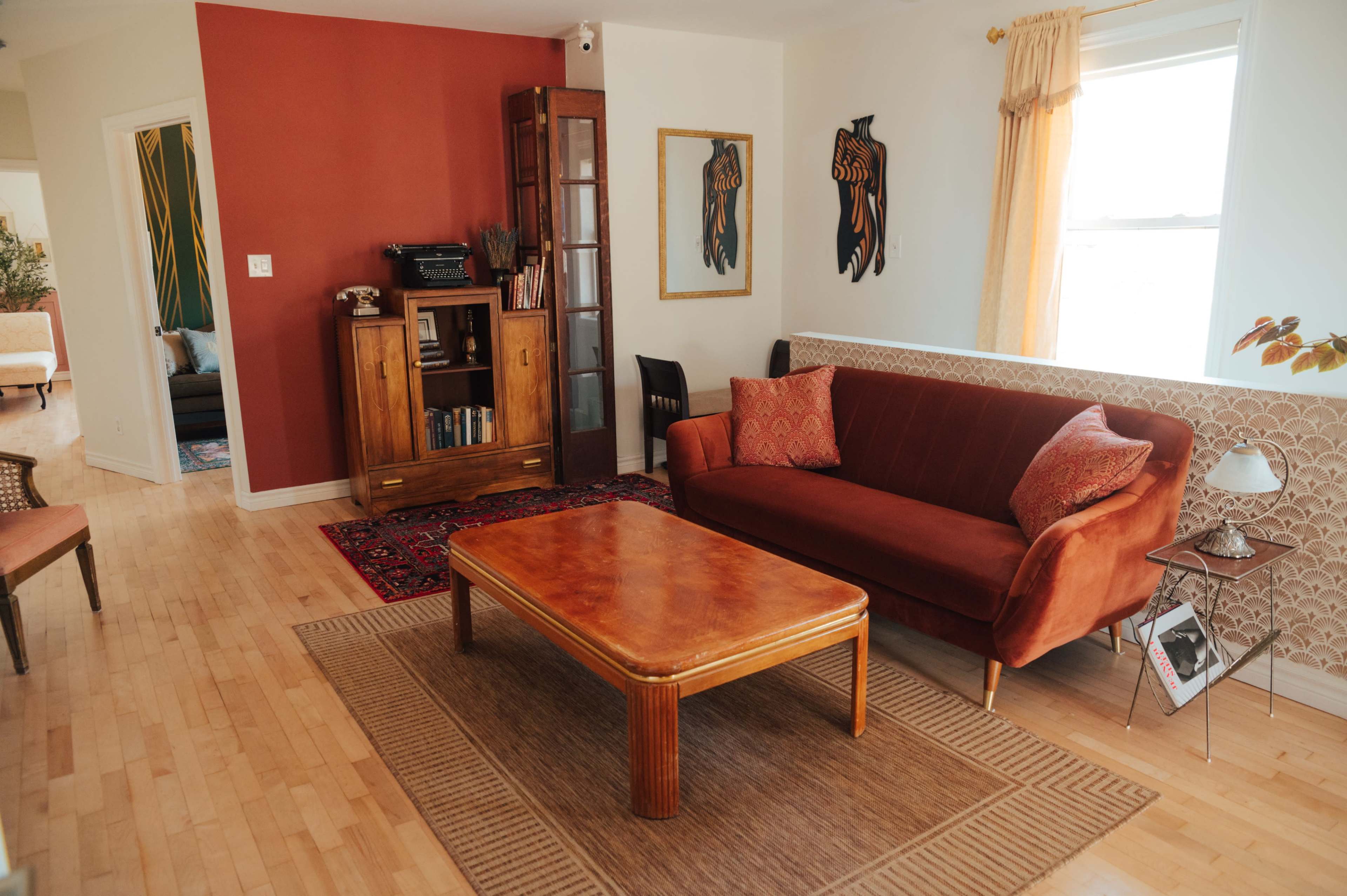 The image shows a living room with a red accent wall, a red velvet sofa, a wooden coffee table, and decorative artwork on the walls.