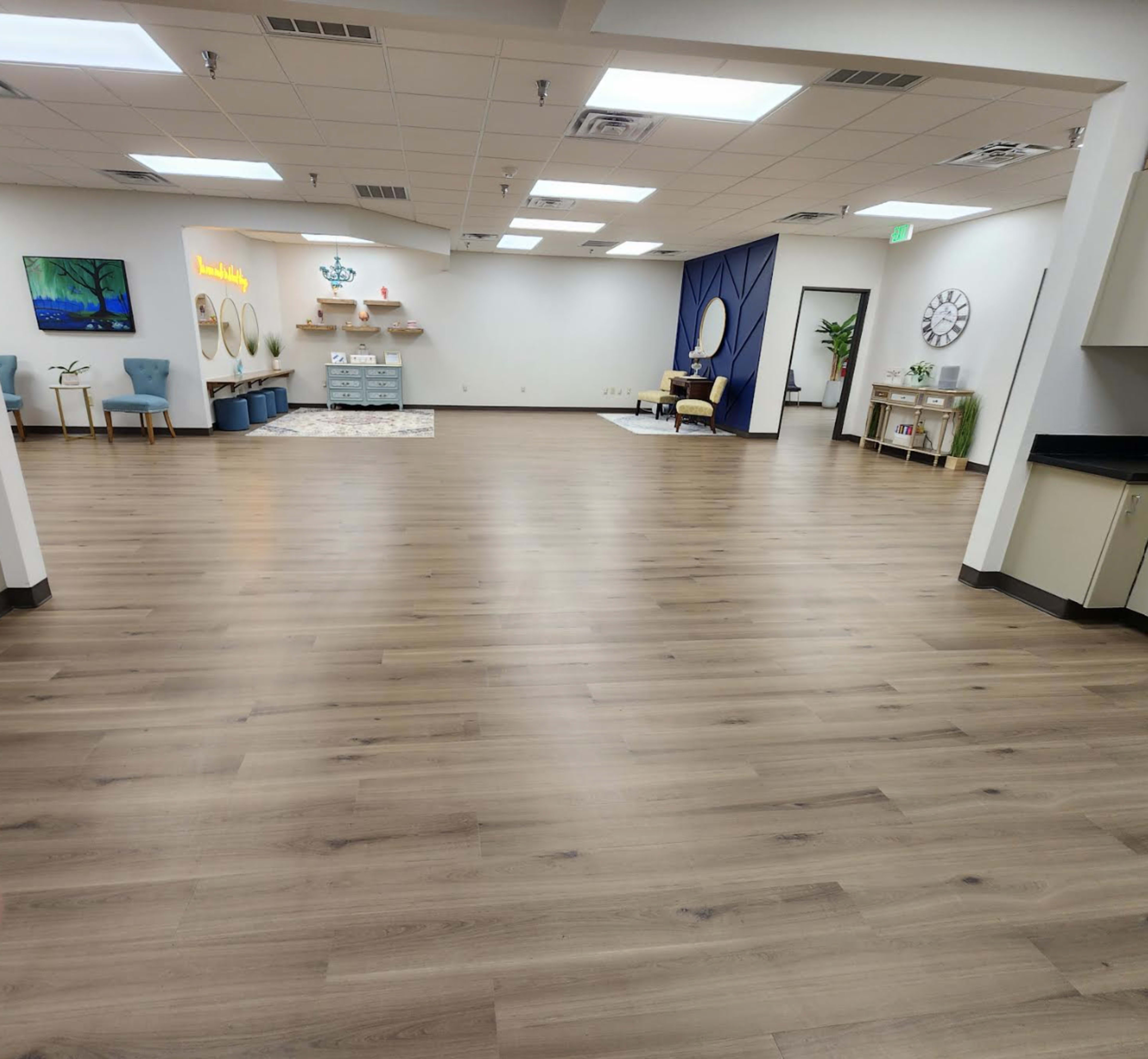 The image shows a spacious, empty room with wooden flooring, a seating area, and decorative elements along the walls.