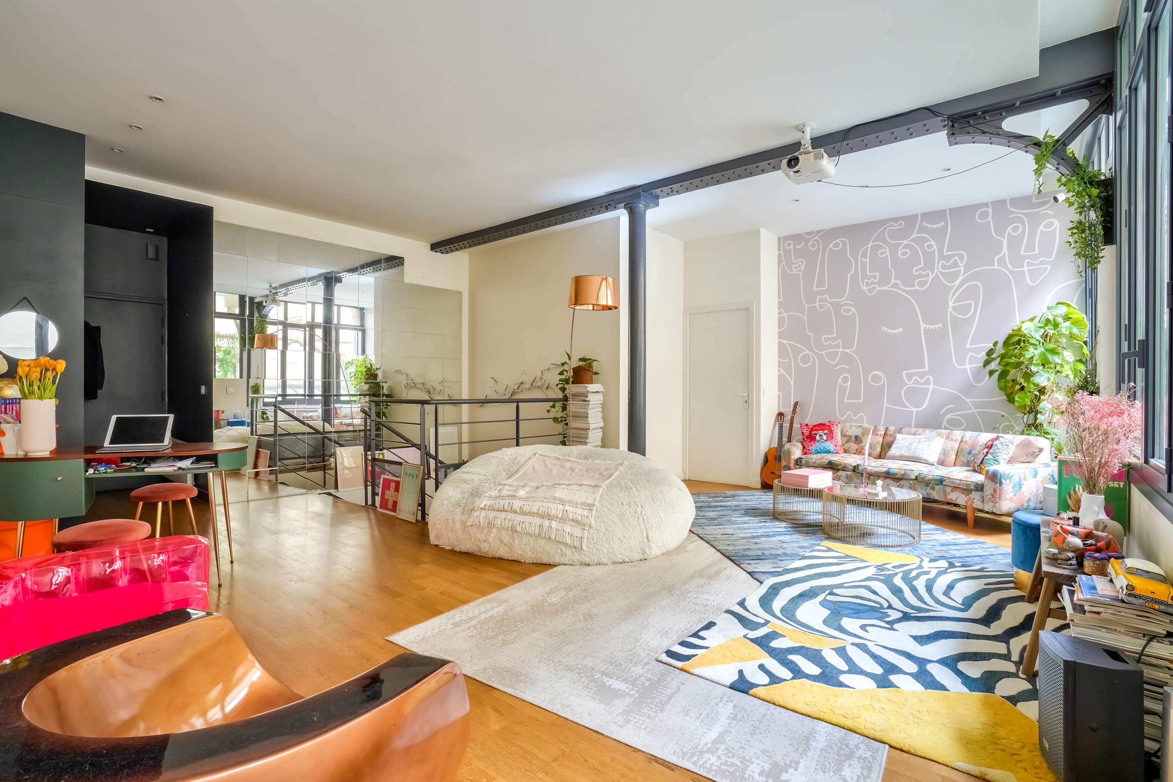 The image shows a modern open-plan living space featuring a cozy seating area, a bean bag, and colorful decor with plants and artwork.