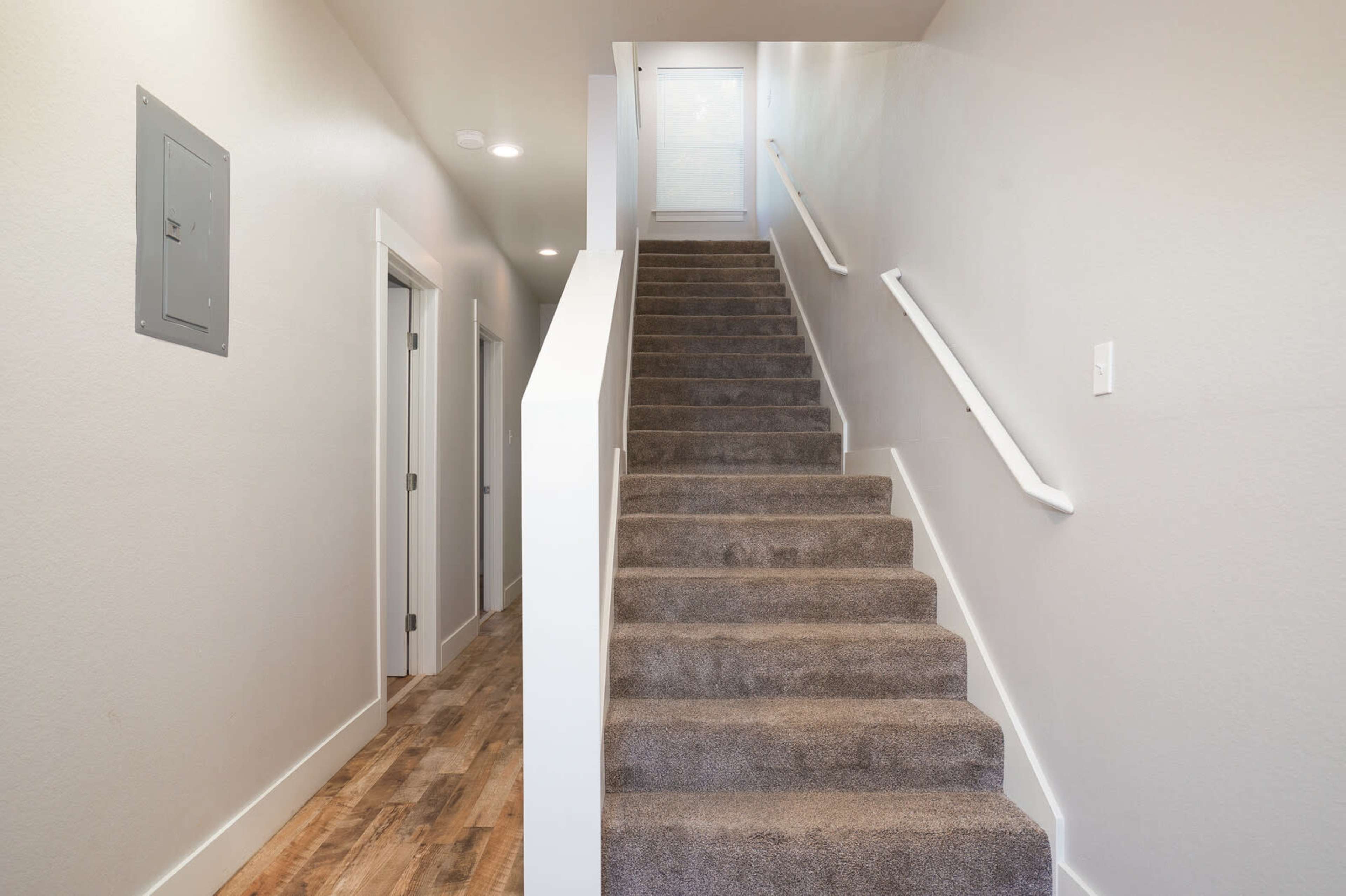 A carpeted staircase leads to a brightly lit landing at the top, with doors lining the walls on either side.
