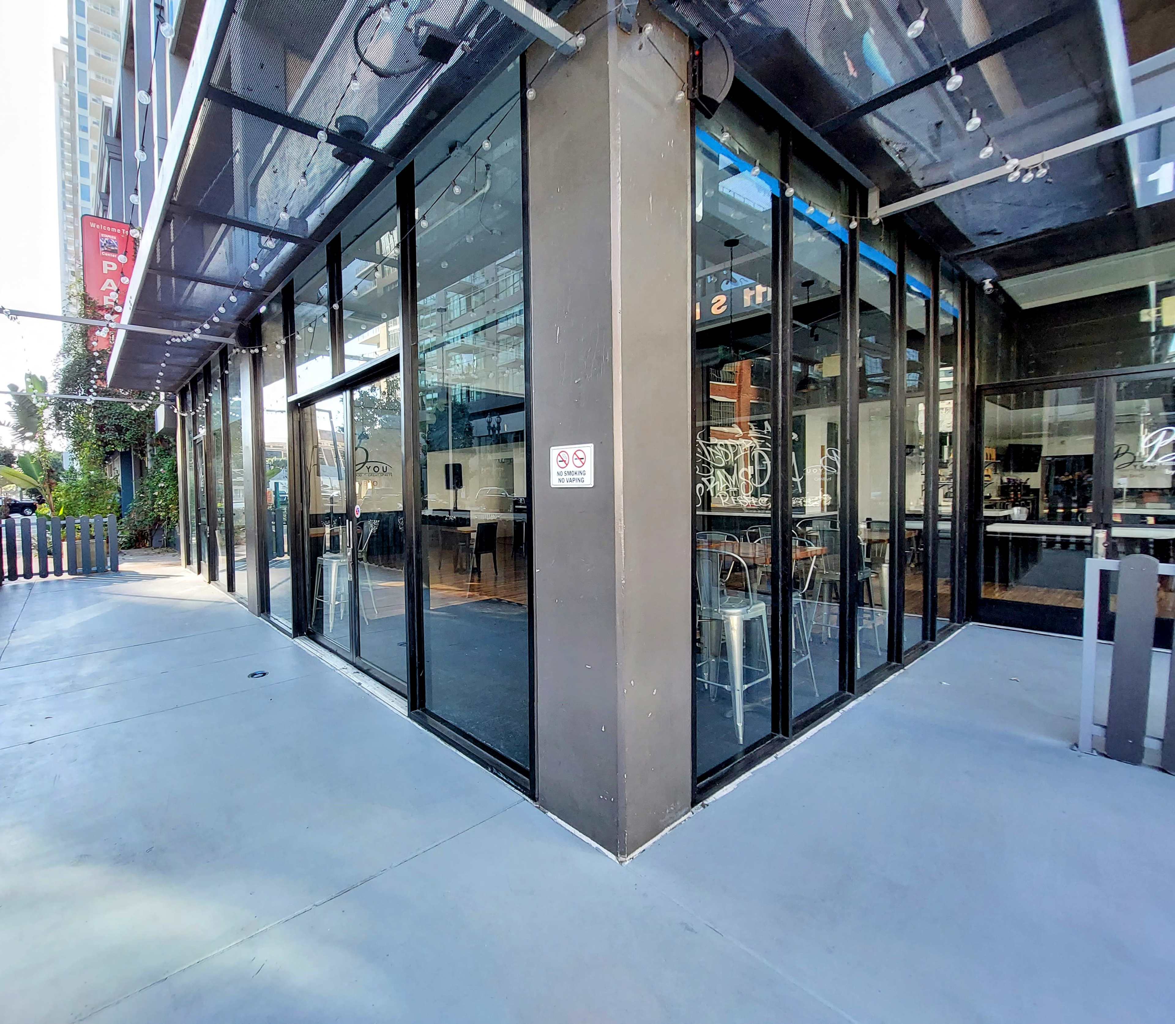 A corner restaurant features large glass windows and a modern exterior, with outdoor seating visible on the sidewalk.